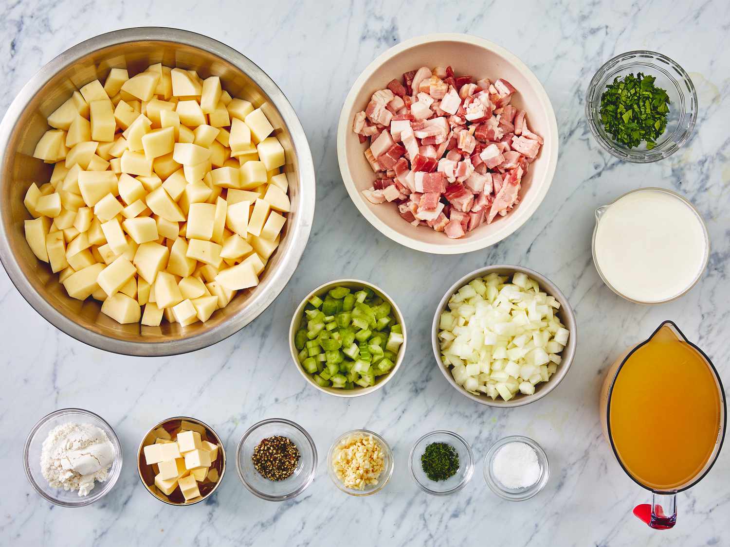 Raw ingredients for cream of potato soup arranged on a kitchen counter including potatoes, onion, garlic, butter, broth, cream, and seasonings