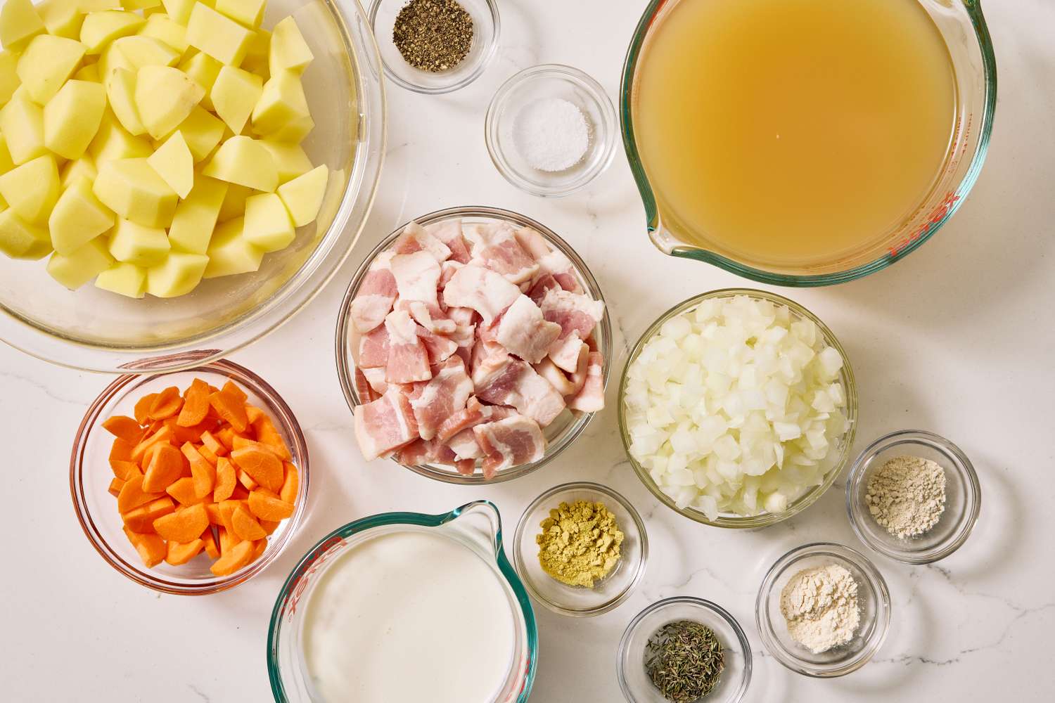 Raw ingredients for slow cooker potato soup arranged on a bright kitchen counter, including russet potatoes, onion, garlic, chicken broth, bacon, cheddar cheese, sour cream, and green onions