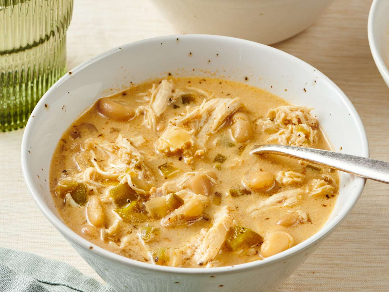 Raw ingredients for white chicken chili arranged on a clean kitchen counter including chicken breasts, white beans, canned green chiles, onion, garlic, broth, spices, cream cheese, lime, and cilantro