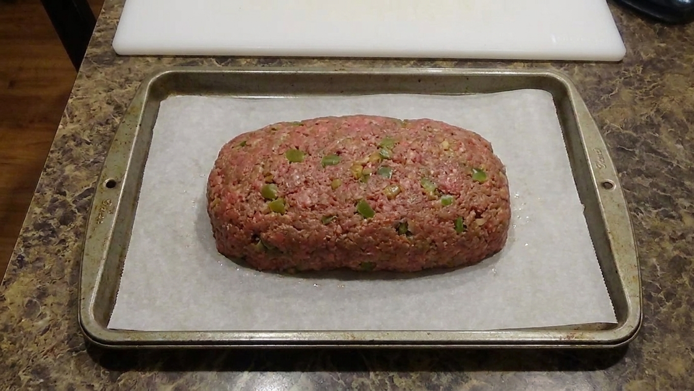 Raw meatloaf shaped into a loaf on a parchment-lined rimmed baking sheet on a kitchen counter