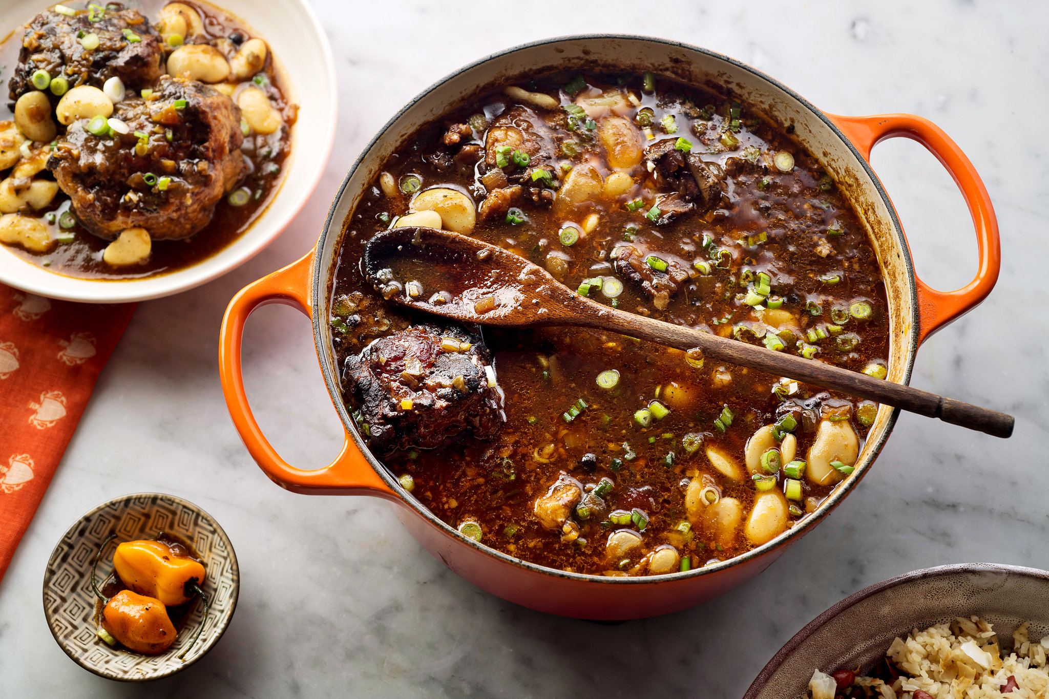 Raw oxtails, butter beans, carrots, onions, garlic, scallions, thyme, Scotch bonnet pepper, soy sauce, browning sauce, and spices arranged on a kitchen counter