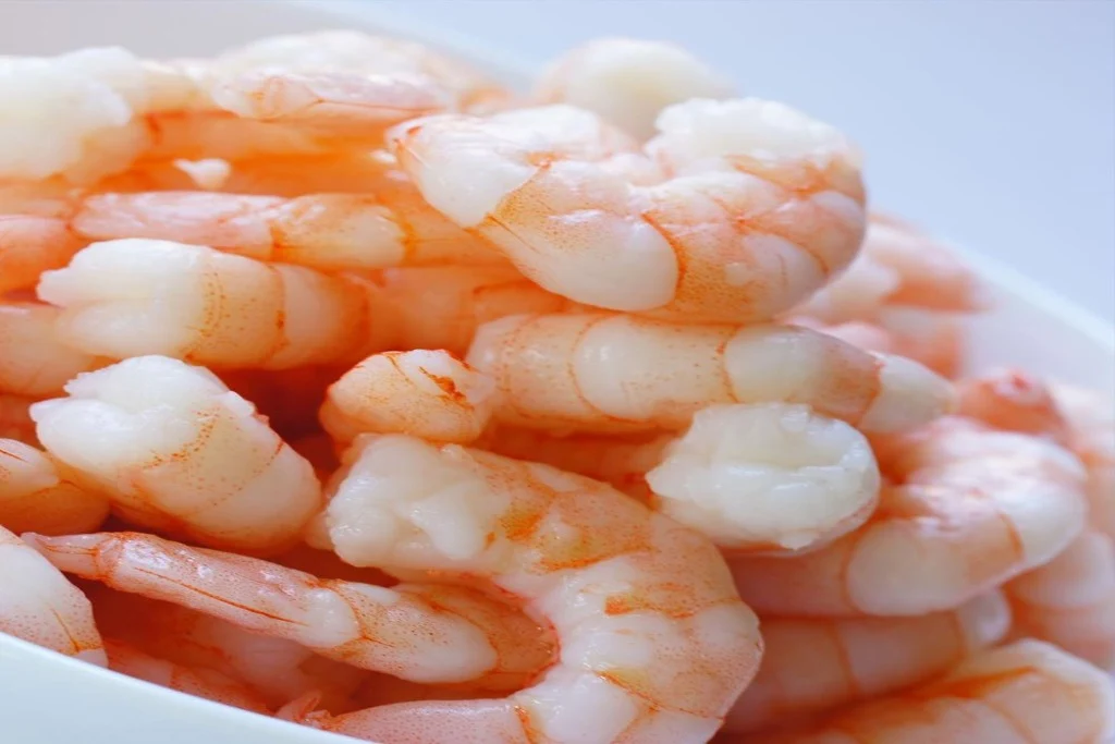Raw peeled and deveined shrimp spread on a cutting board with paper towels and a small bowl of salt nearby