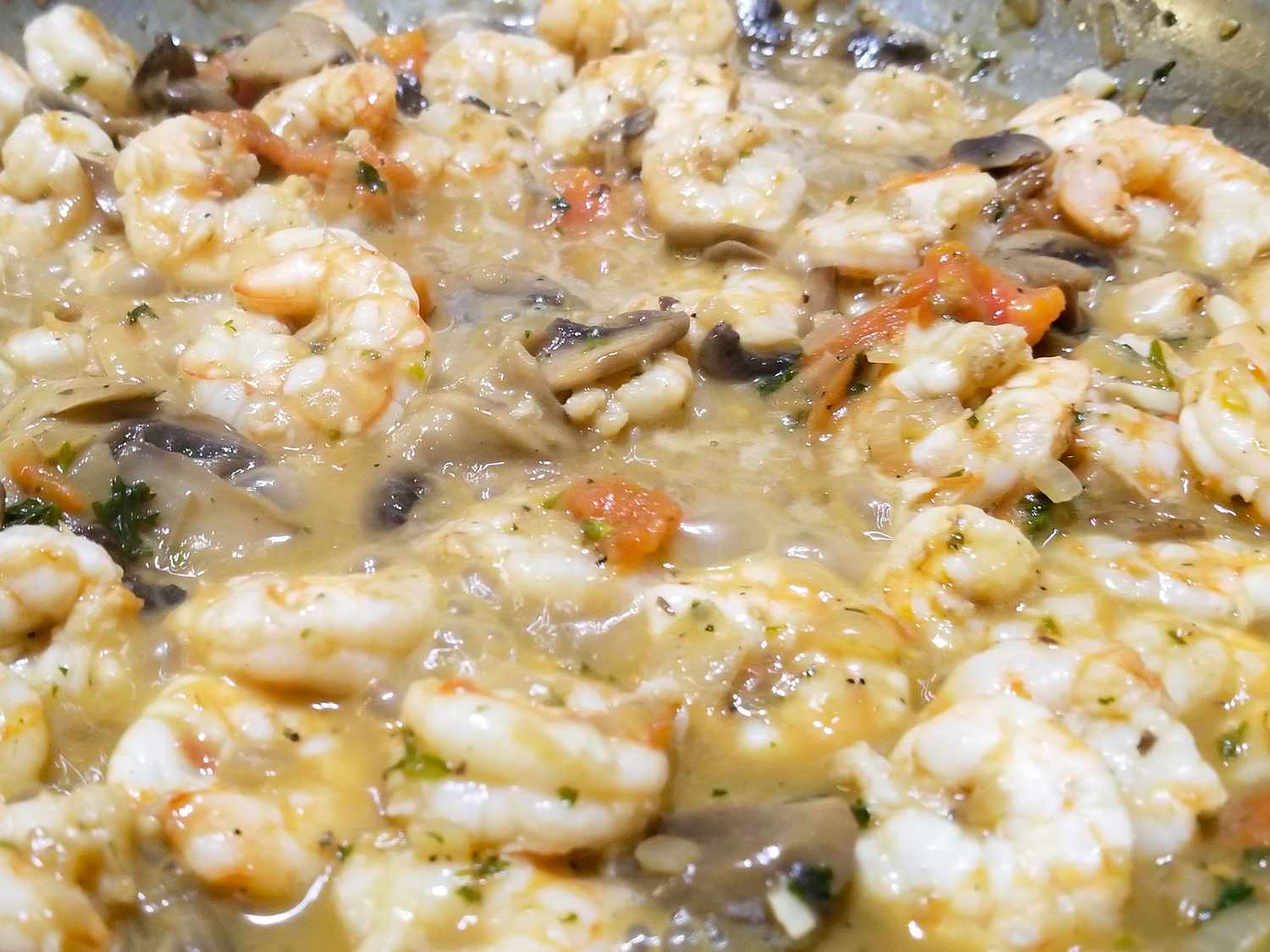 Raw peeled shrimp, sliced mushrooms, limes, cilantro, and fish sauce arranged on a clean kitchen counter ready for cooking