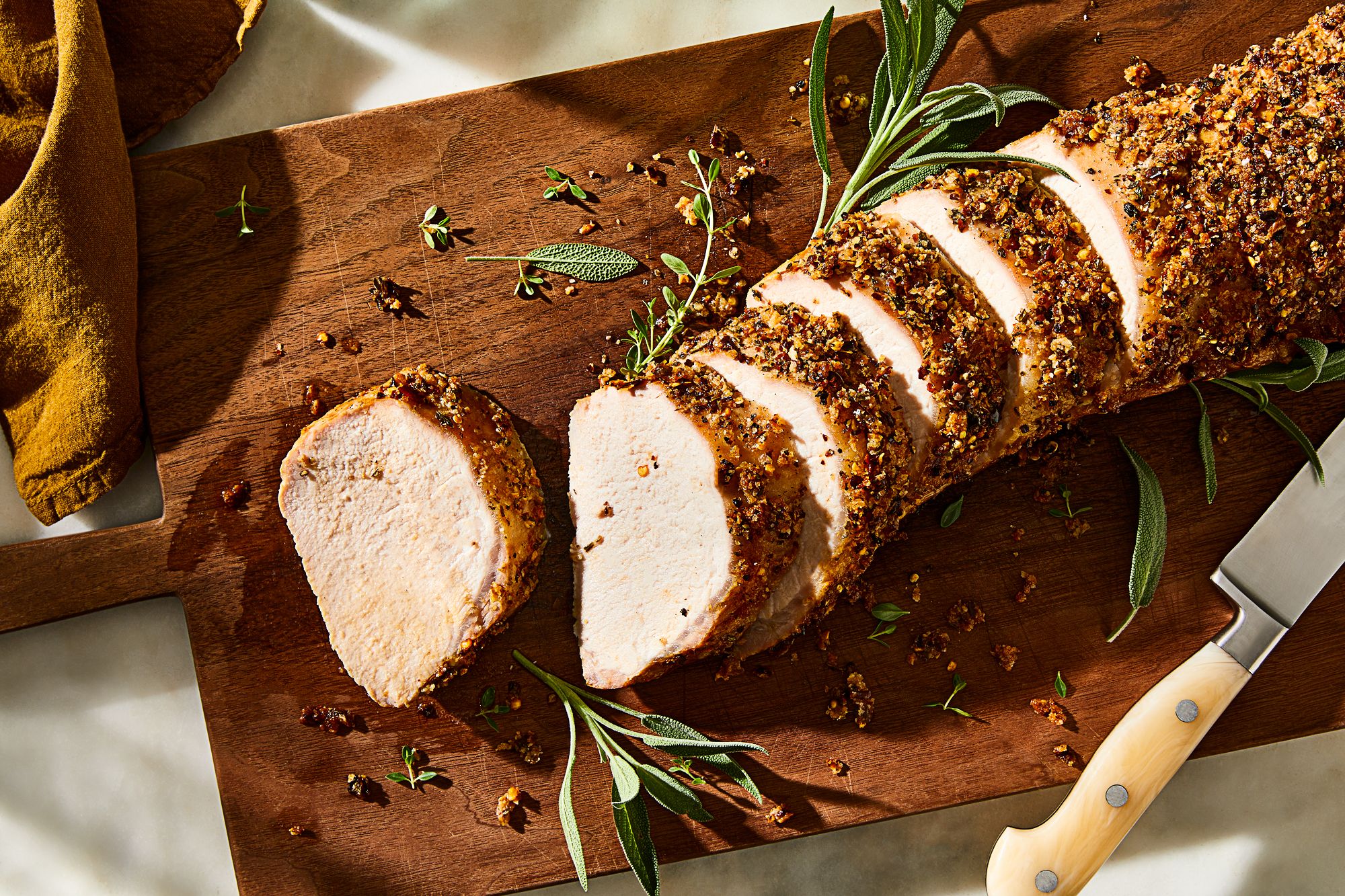 Raw pork loin roast, garlic, rosemary, thyme, Dijon mustard, olive oil, salt, pepper, carrots, onion, and chicken broth arranged on a kitchen counter