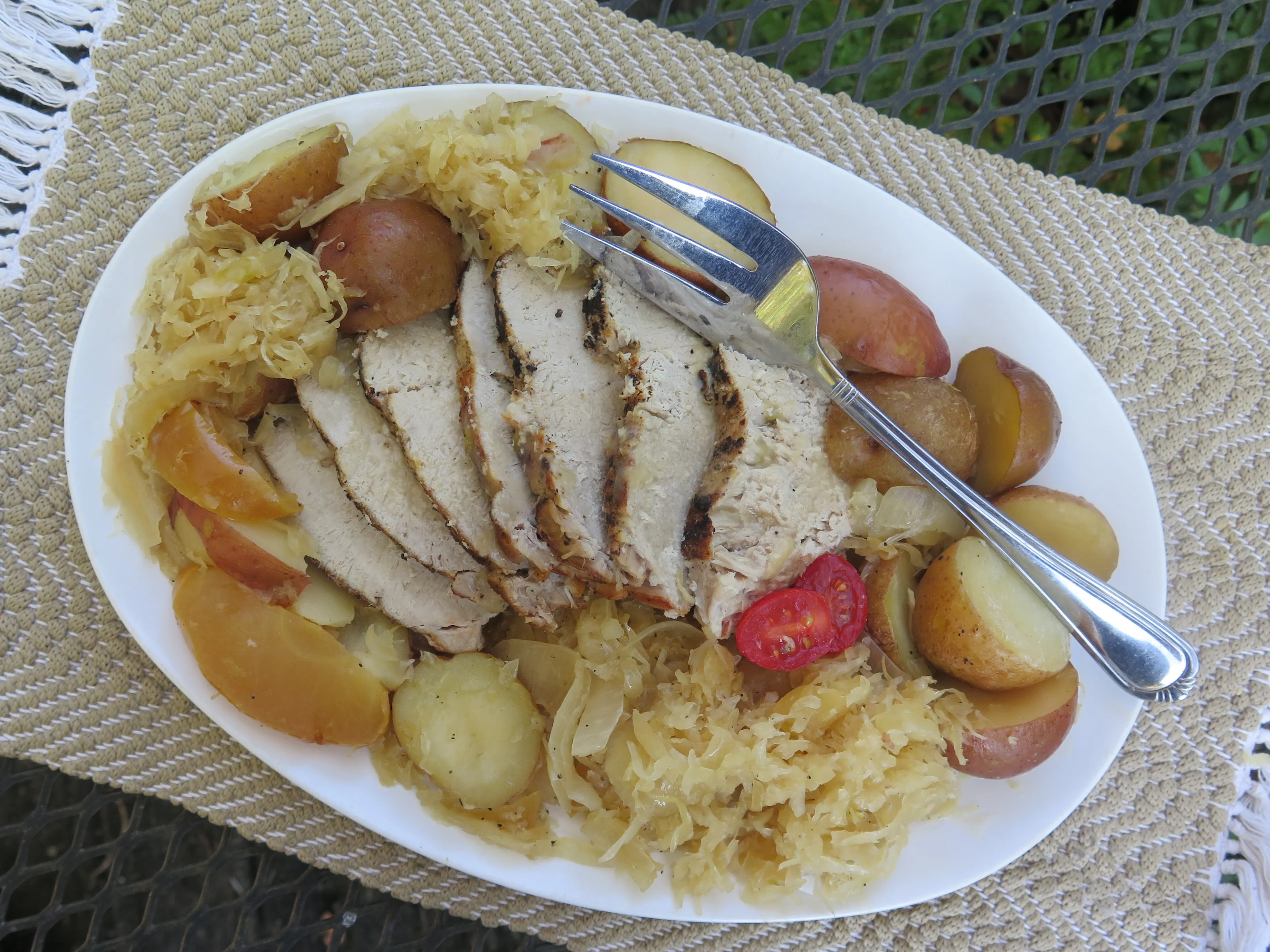 Raw pork roast, a jar of sauerkraut, sliced apples, onion, garlic, caraway seeds, and broth measured on a clean kitchen counter