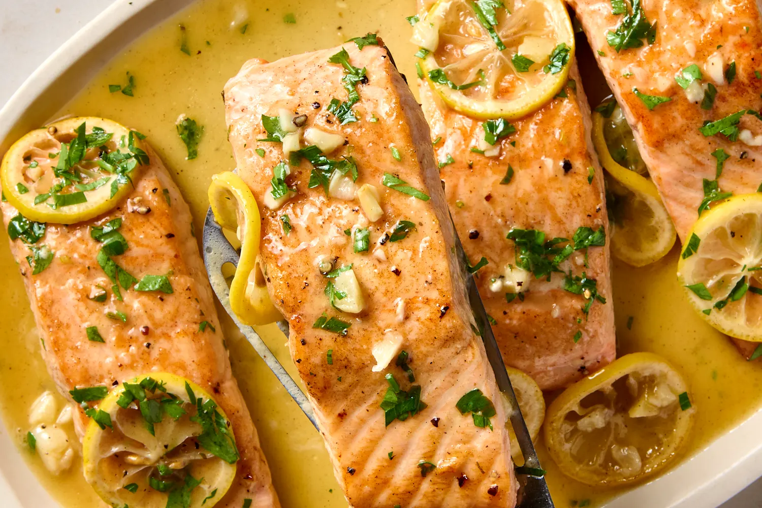 Raw salmon fillets on a cutting board with small bowls of paprika, garlic powder, salt, pepper, olive oil, and a lemon on a tidy kitchen counter in soft daylight