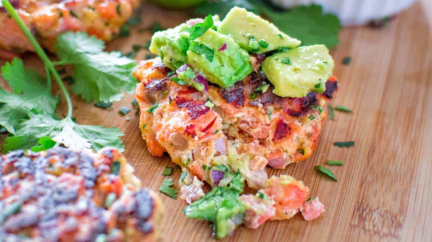 Raw salmon, lemon, dill, breadcrumbs, egg, Dijon mustard, mayonnaise, and burger buns arranged on a clean kitchen counter in consistent warm natural light