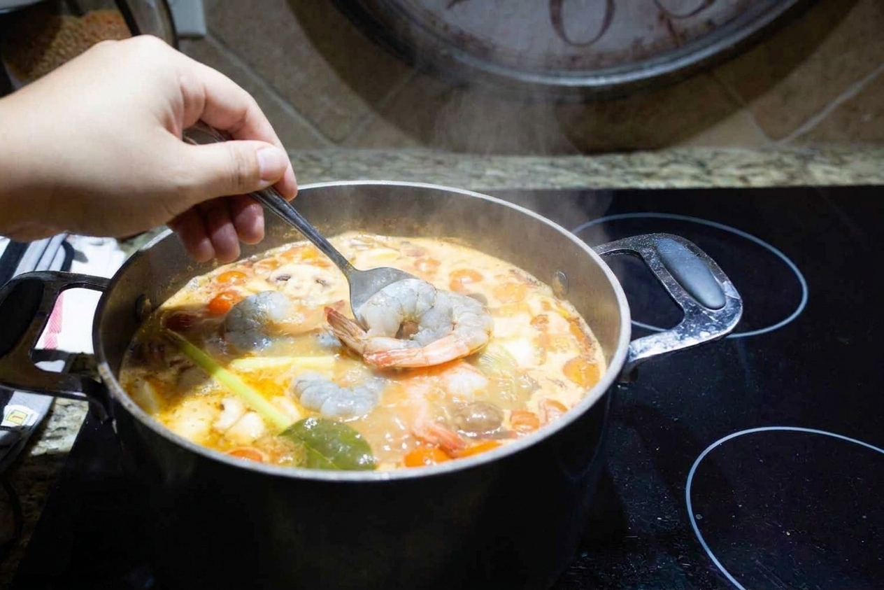 Raw shrimp turning pink while gently cooking in hot tom yum broth in a pot on the stove