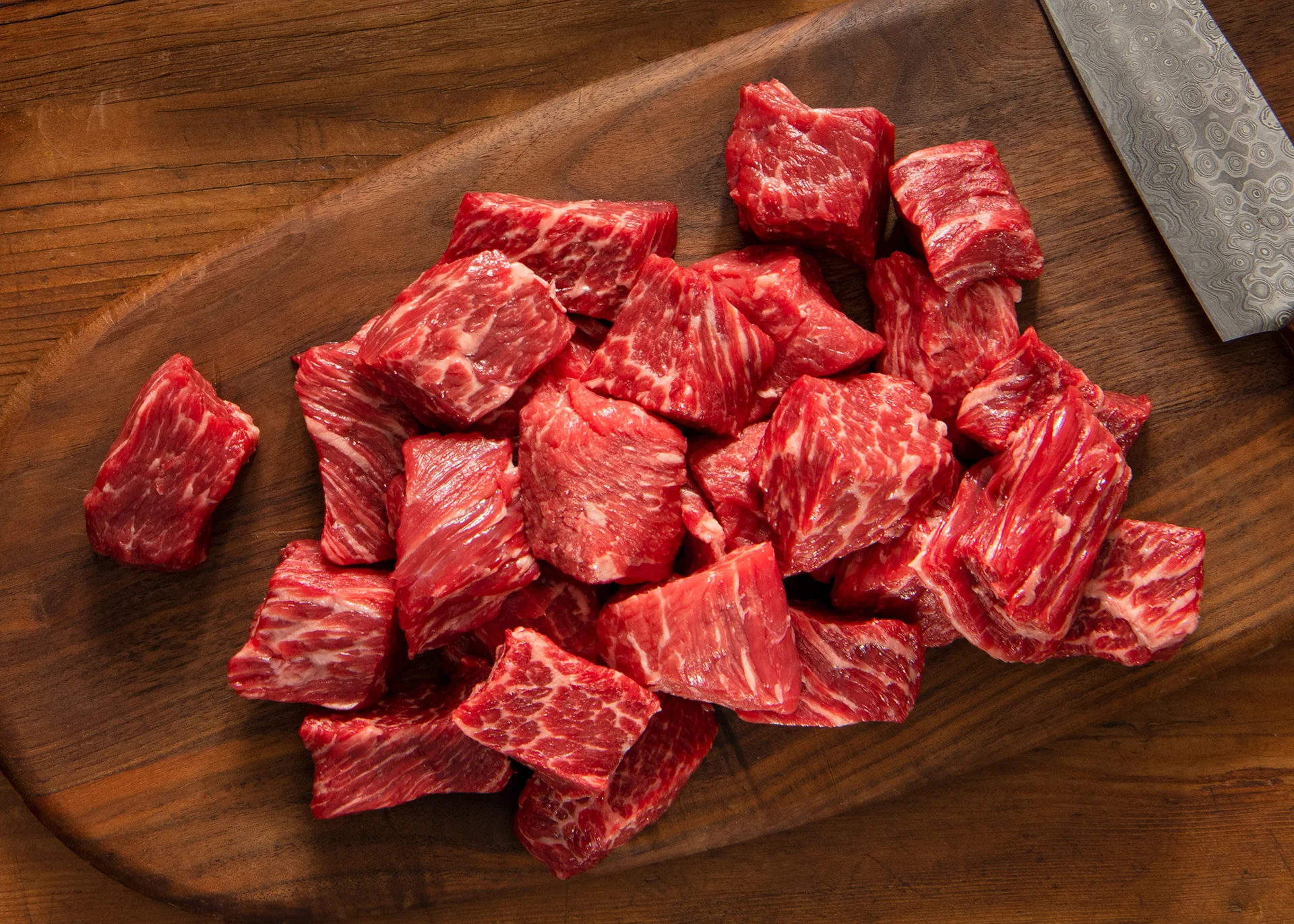 Raw sirloin tip steak cut into even bite-size cubes on a wooden cutting board with a chef's knife nearby