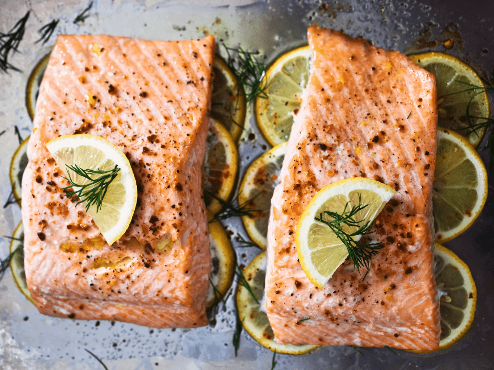 Raw sockeye salmon fillets, butter, lemon, capers, garlic, parsley, salt, pepper, and olive oil arranged on a wooden cutting board on a bright kitchen counter