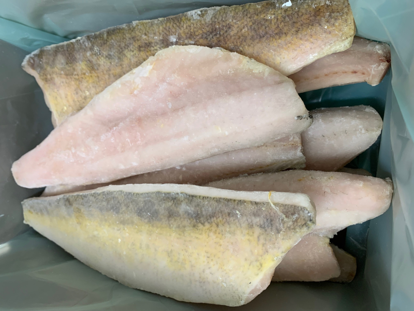 Raw walleye fillets on a cutting board with lemon, capers, parsley, and small bowls of salt and pepper on a clean kitchen counter
