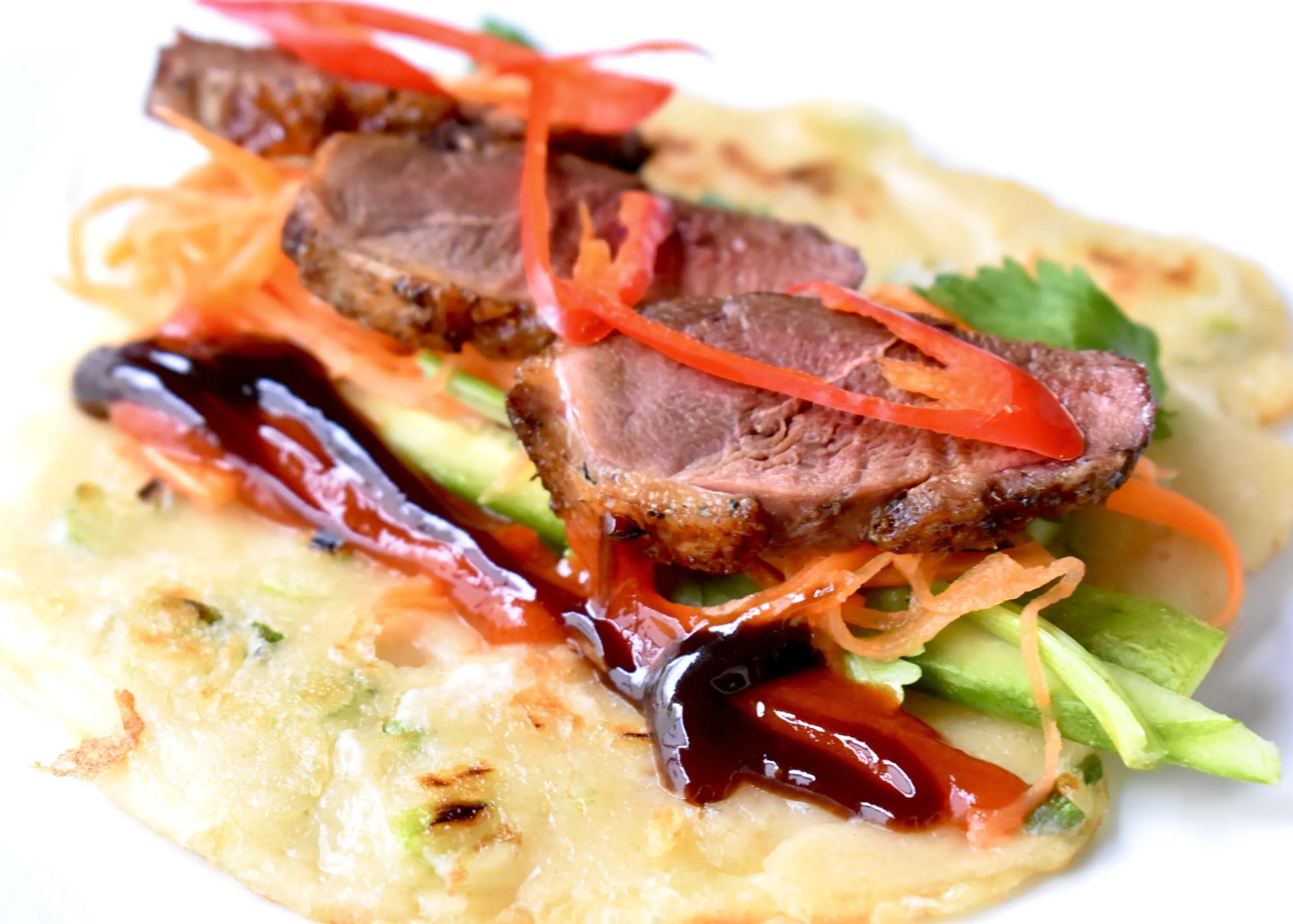 Raw whole duck on a sheet pan next to bowls of hoisin sauce, honey, soy sauce, five-spice, grated ginger, and bundles of scallions and cucumbers on a clean kitchen counter