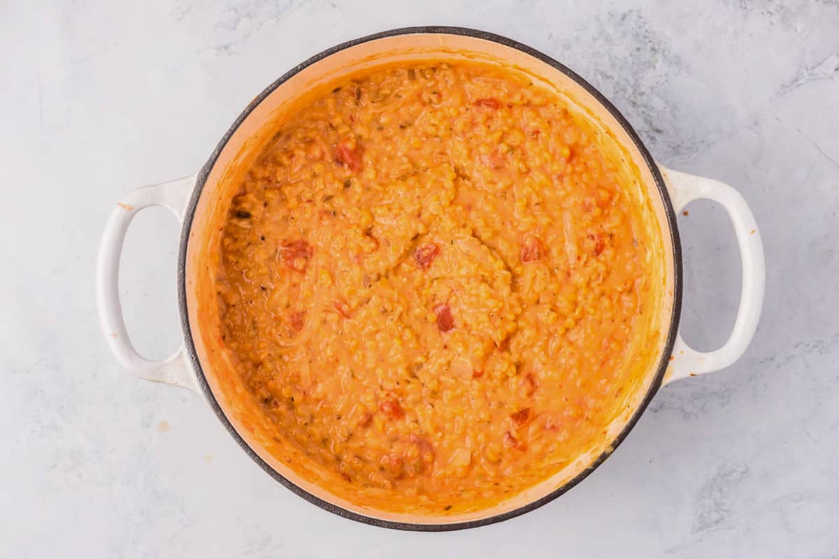 Red lentil dahl simmering in a Dutch oven on a stovetop with a wooden spoon resting on the rim
