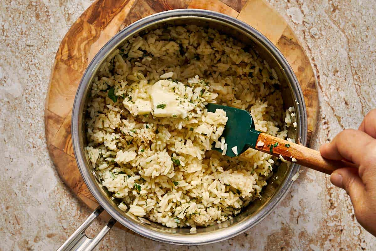 Rice being stirred in a pot with melted garlic butter, showing glossy grains as they toast
