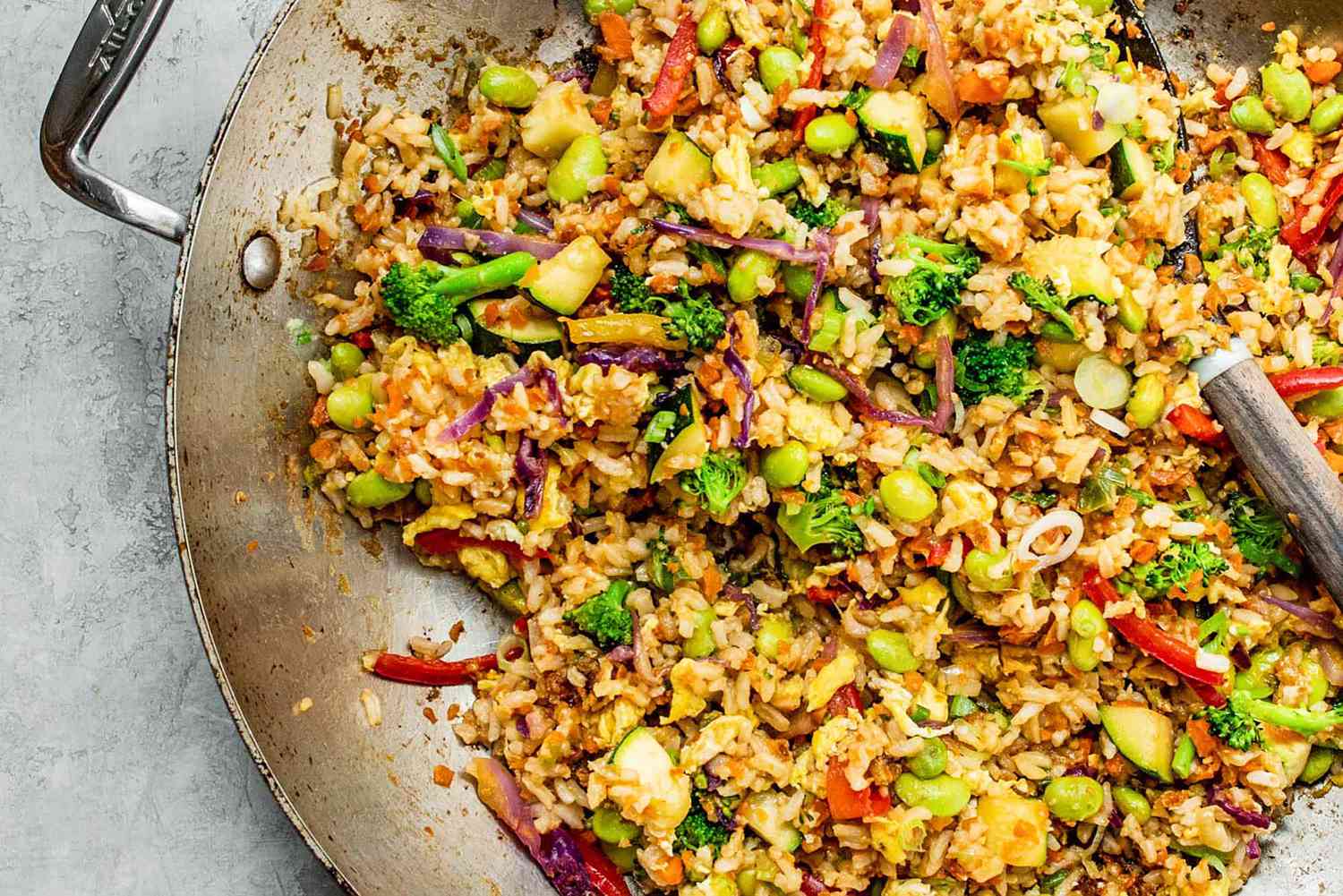 Rice, vegetables, and scrambled egg being stirred together in a hot skillet on a stovetop as steam rises