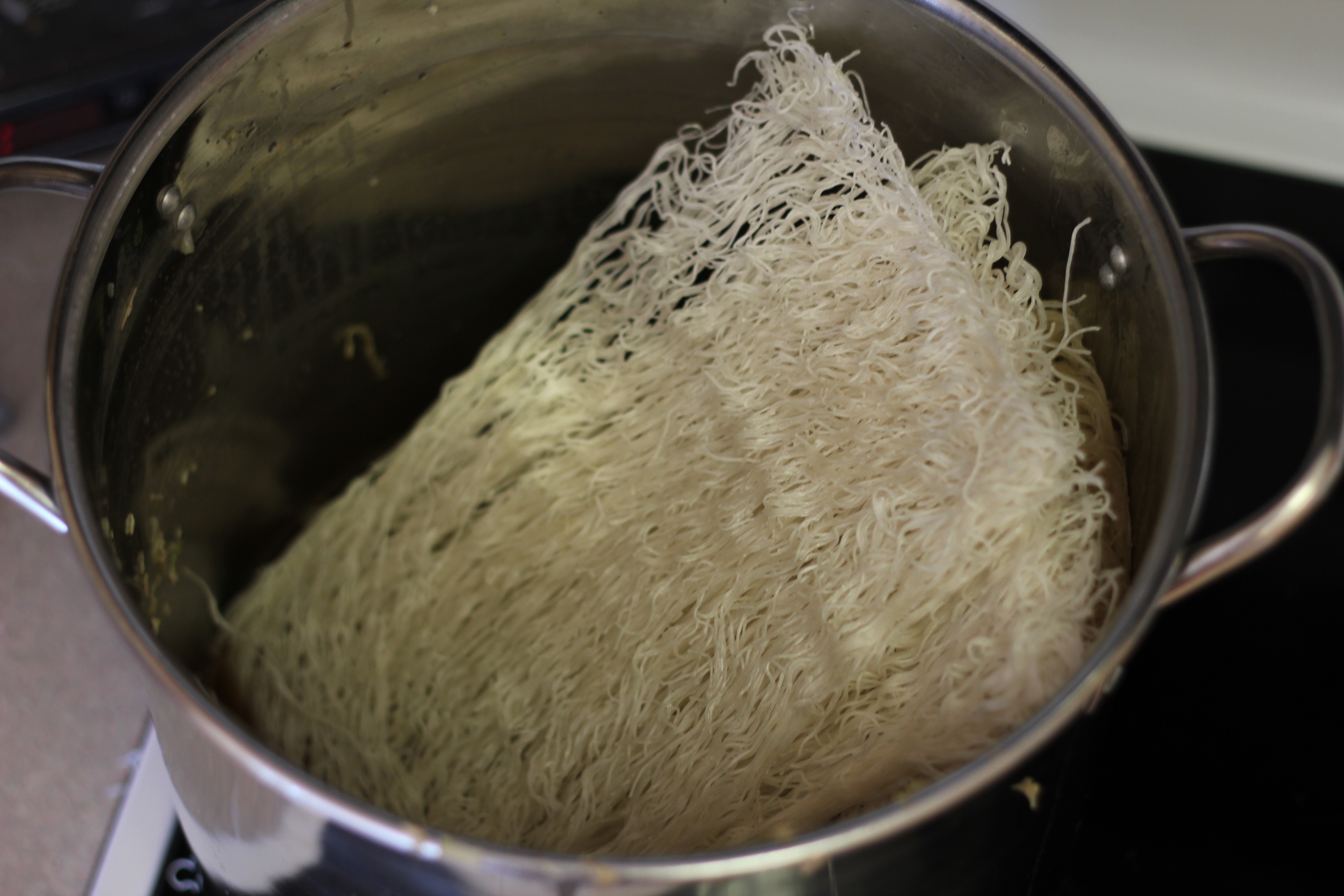 Rice vermicelli noodles soaking in a bowl of warm water on a kitchen counter with tongs resting nearby