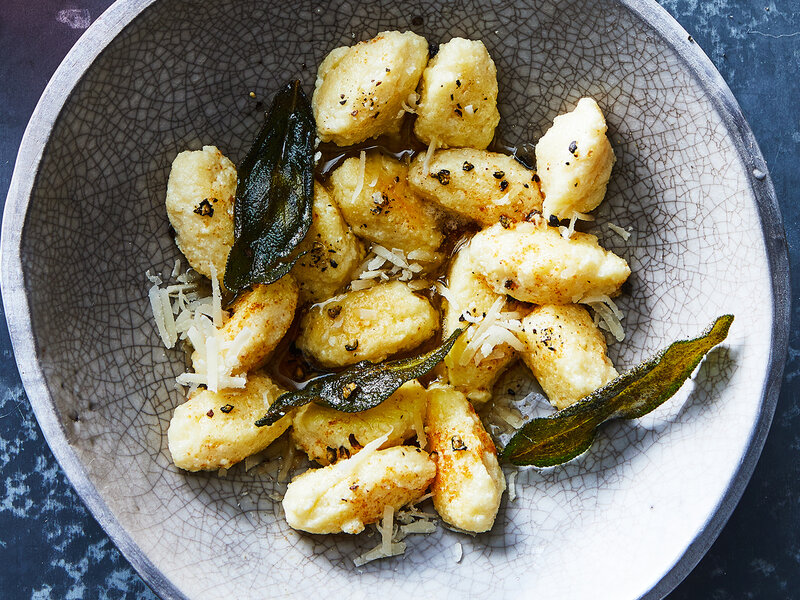 Ricotta, grated Parmesan, an egg, flour, salt, and pepper arranged on a clean kitchen counter with a mixing bowl nearby in soft natural light