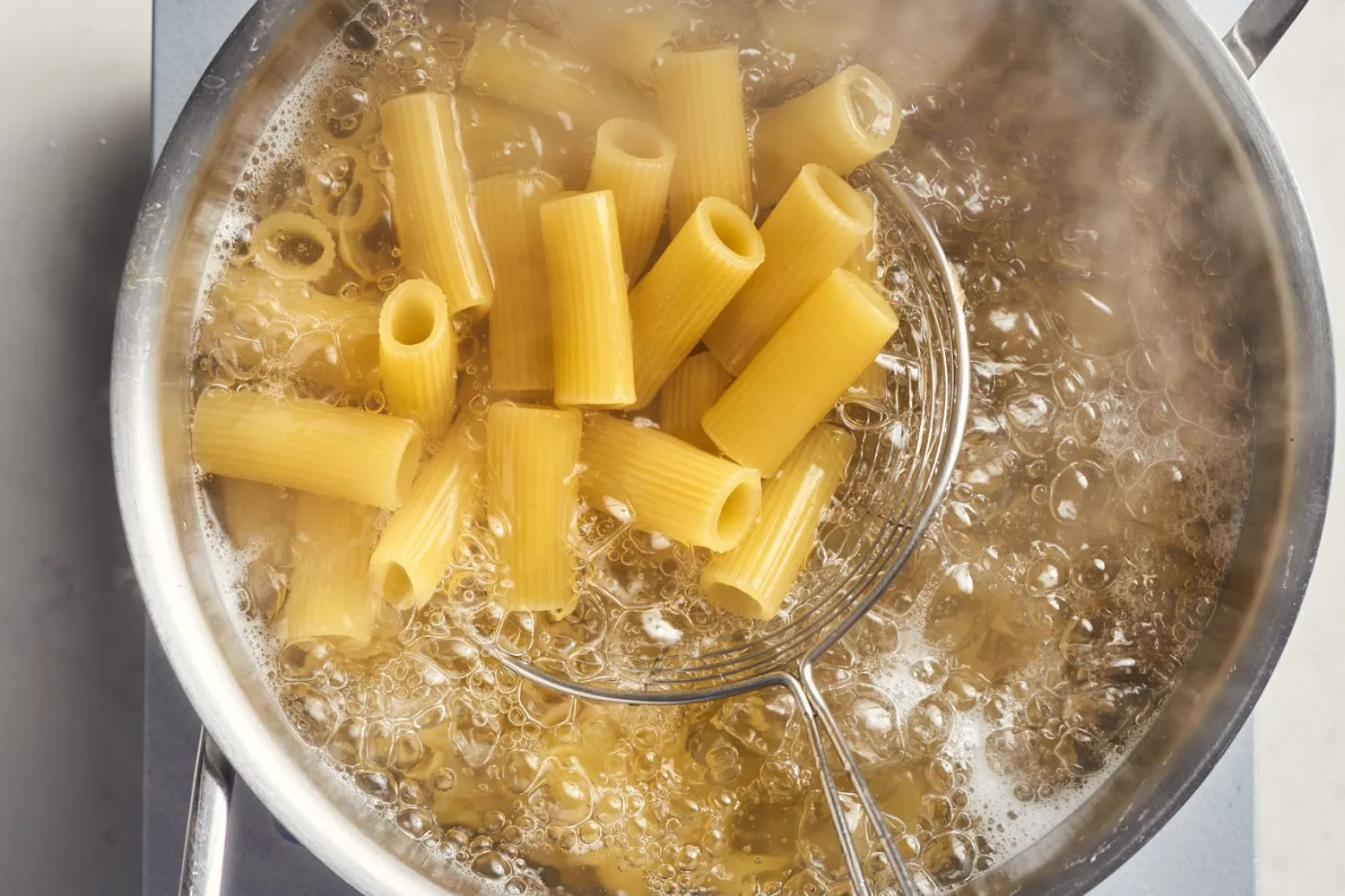 Rigatoni boiling in a large pot of salted water on a stovetop, steam rising