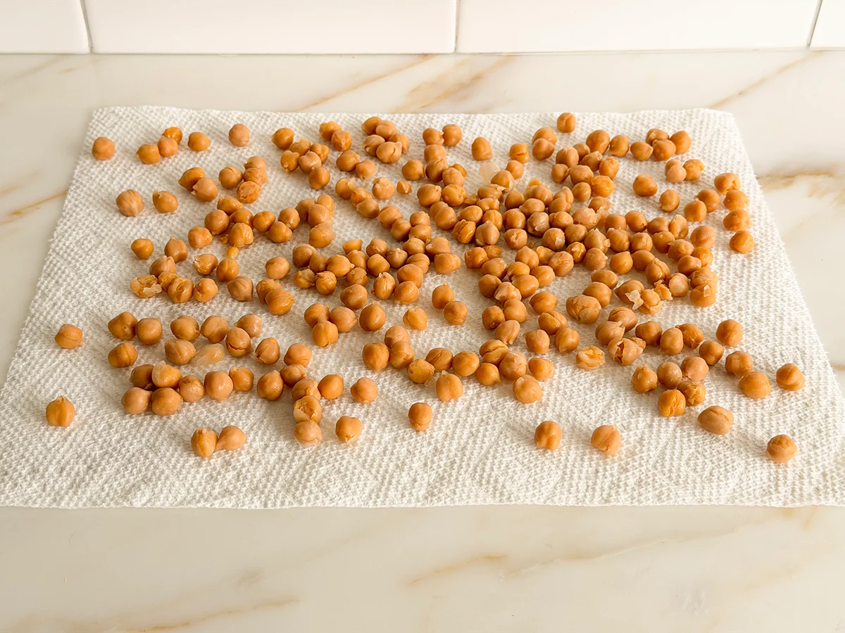 Rinsed chickpeas spread on a clean kitchen towel on a countertop, ready to be dried before roasting