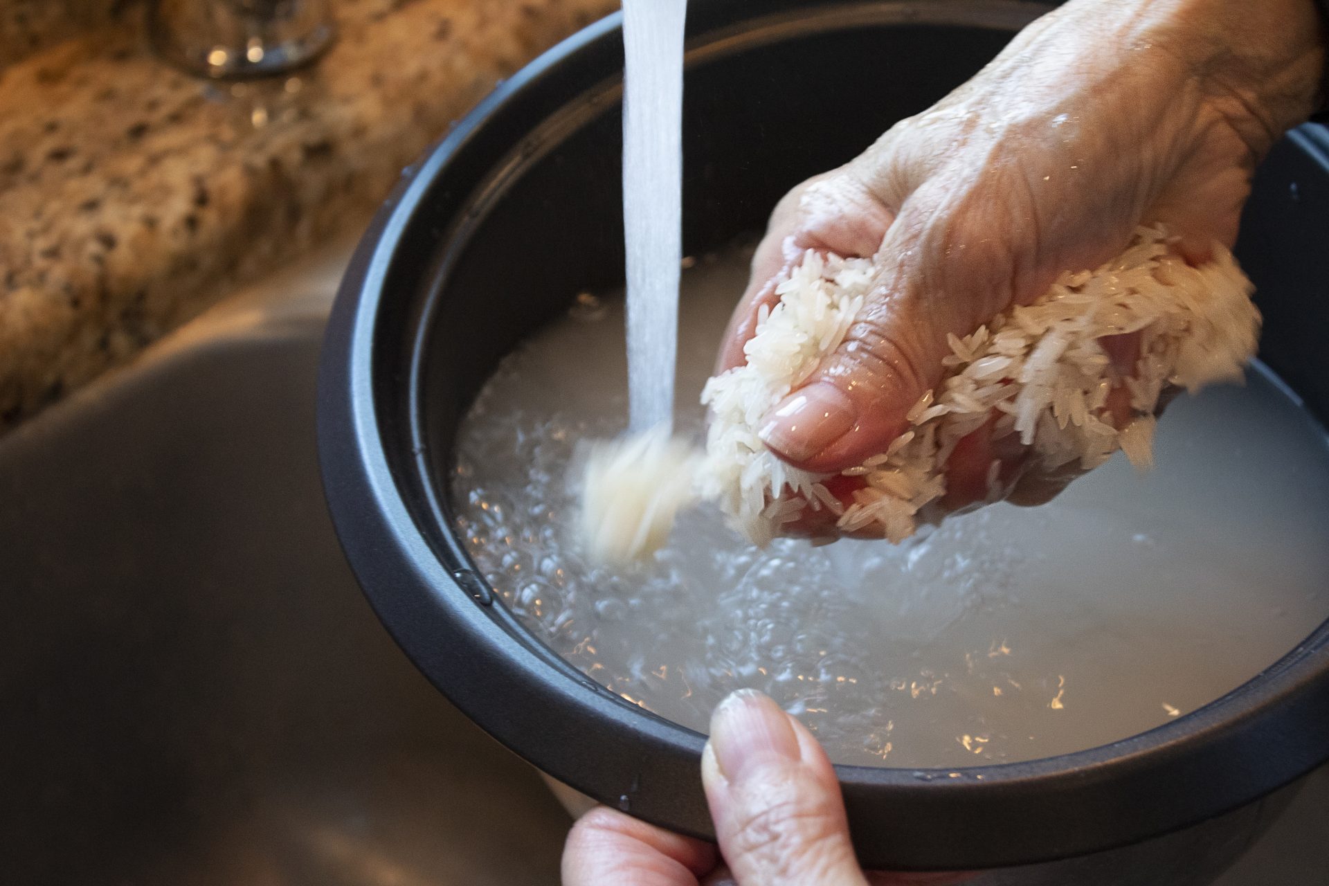 Rinsed jasmine rice draining in a fine mesh strainer over a bowl in a home kitchen sink