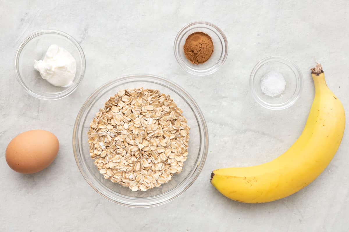 Ripe bananas, rolled oats, eggs, cinnamon, baking powder, and milk arranged on a clean kitchen counter ready for pancake prep