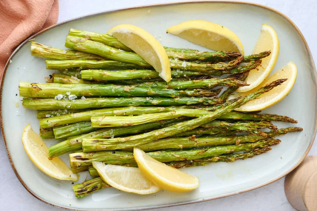 Roasted asparagus on a serving platter with lemon wedges and flaky salt