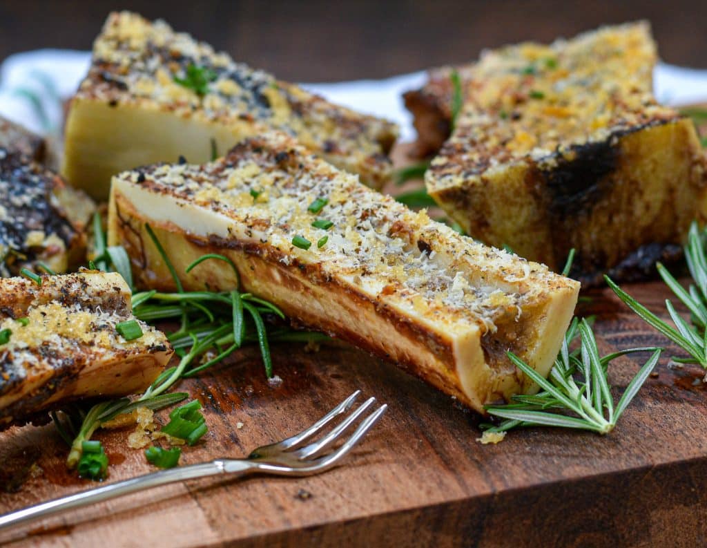 Roasted beef marrow and knuckle bones on a rimmed baking sheet, deeply browned with caramelized bits, resting on a kitchen counter