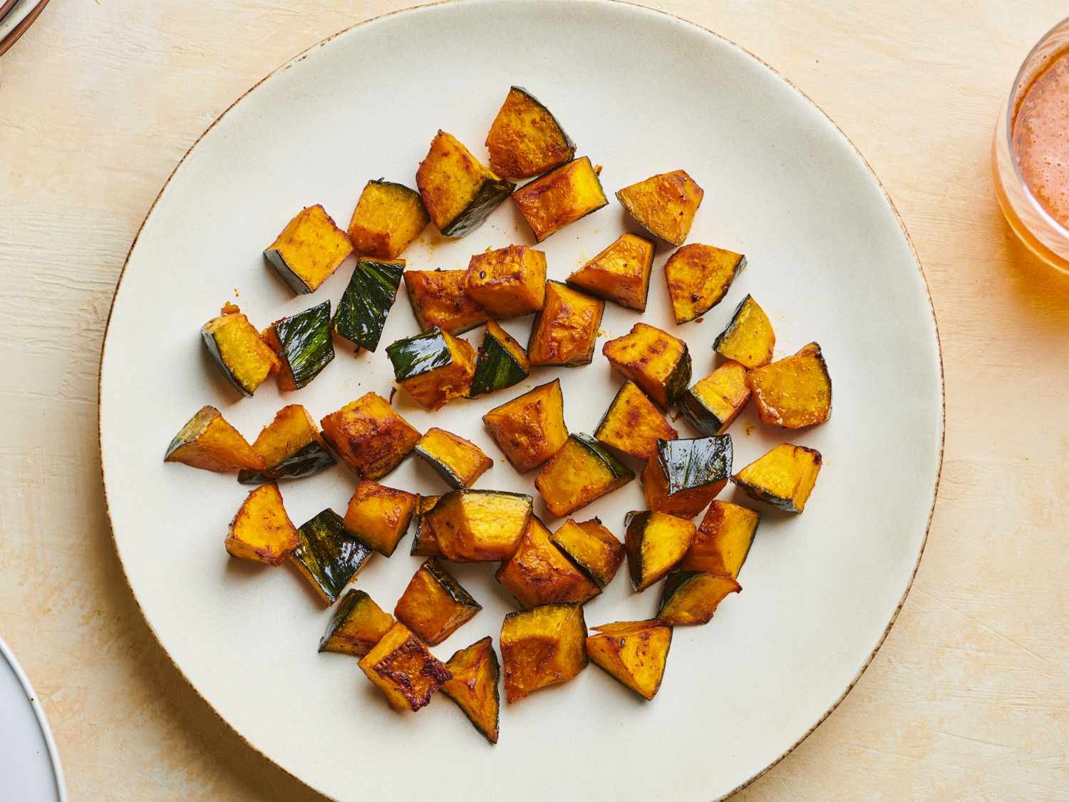Roasted kabocha squash wedges plated on a ceramic dish with maple miso butter drizzled on top, garnished with sesame seeds and scallions on a dining table