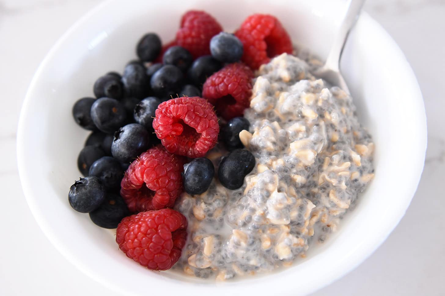 Rolled oats, chia seeds, and fresh mixed berries in separate bowls on a bright kitchen counter