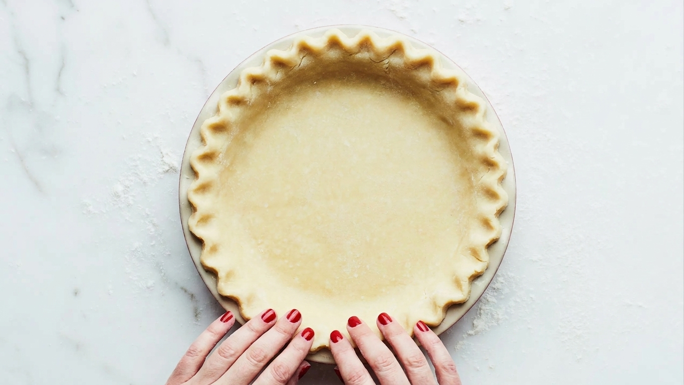 Rolled pie dough fitted into a ceramic pie plate with a neat crimped edge on a bright kitchen counter