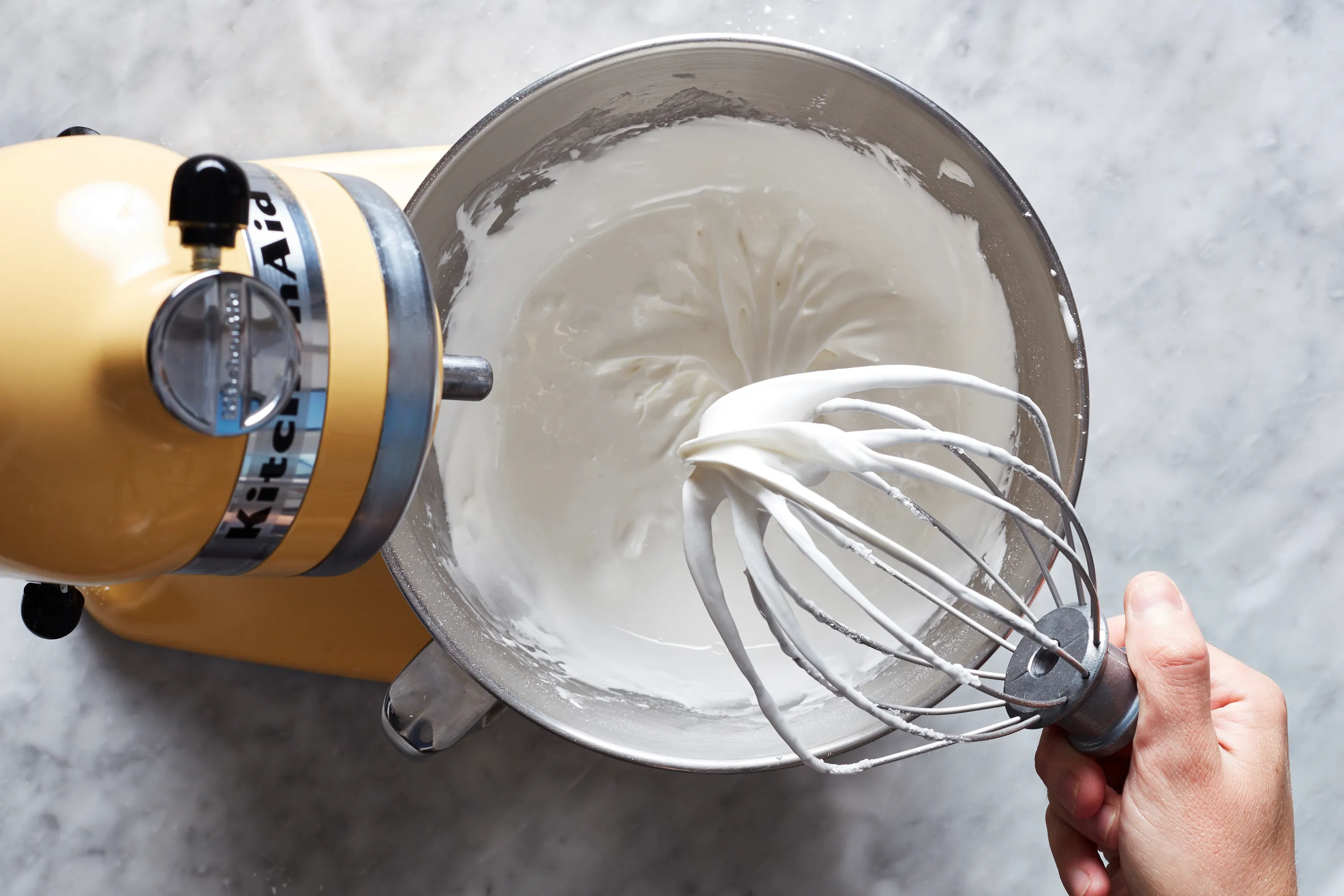 Royal icing being mixed in a stand mixer bowl with a whisk attachment on a bright kitchen counter