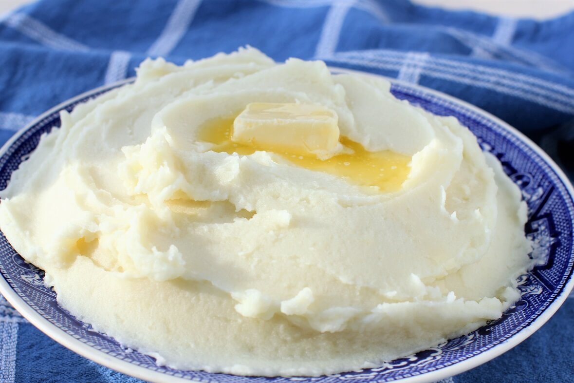 Russet potatoes, a bowl of flour, butter, salt, and a small pitcher of heavy cream arranged and ready for lefse