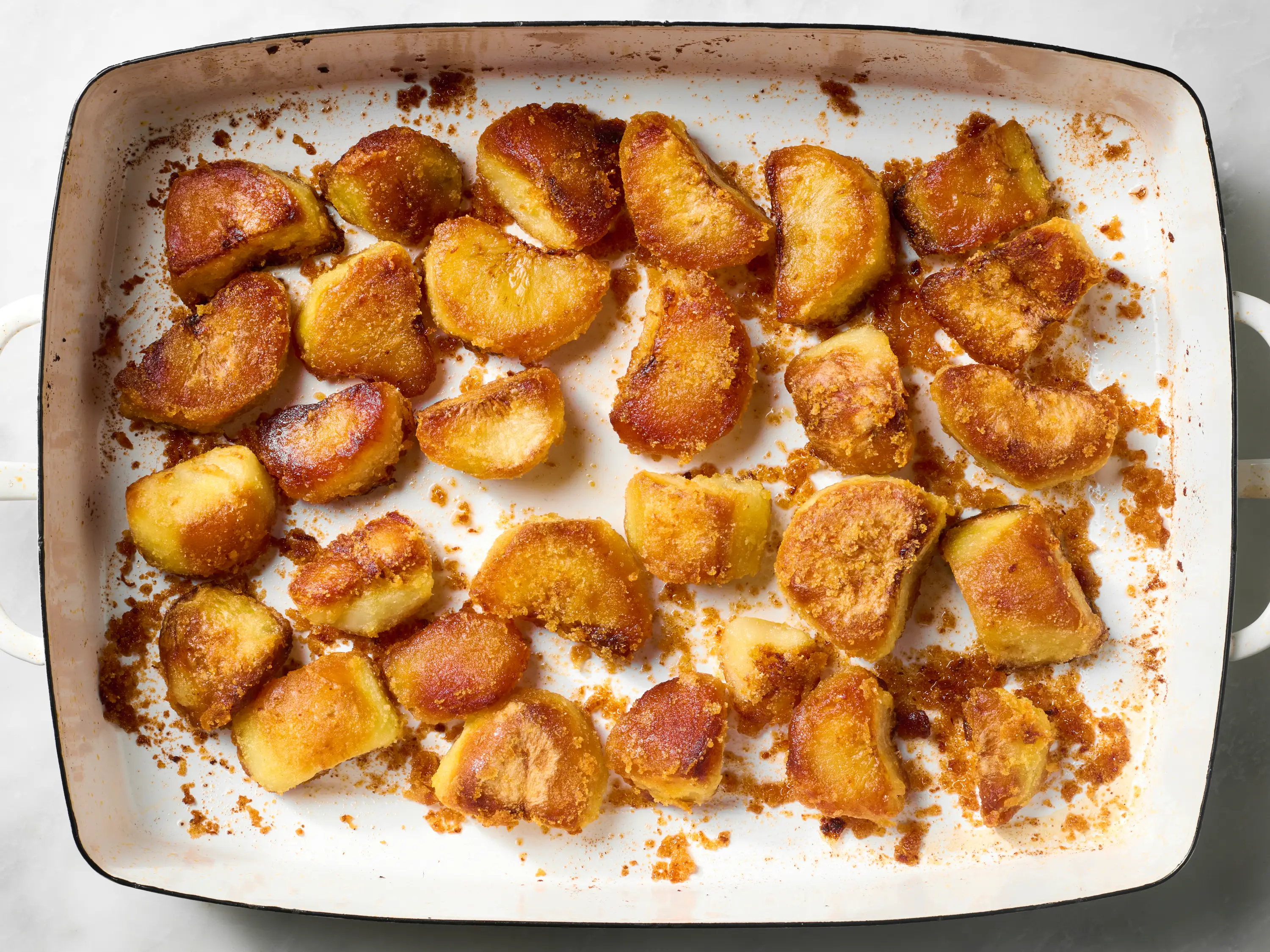 Russet potatoes, kosher salt, baking soda, and a bottle of olive oil arranged on a clean kitchen counter with a large pot nearby
