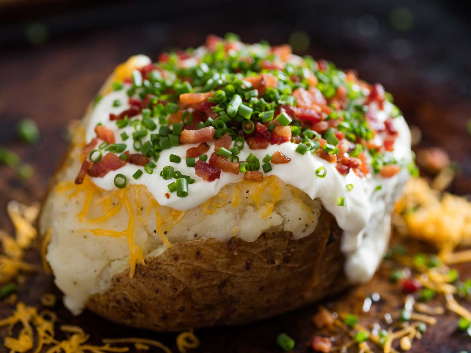 Russet potatoes, shredded cheddar, sour cream, milk, butter, onion, garlic, and seasonings arranged on a kitchen counter in natural light