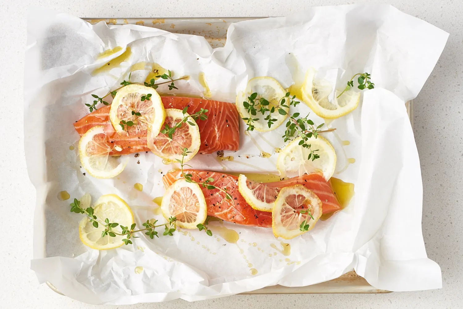 Salmon fillets on parchment lined sheet pan being patted dry with paper towels on a home kitchen counter