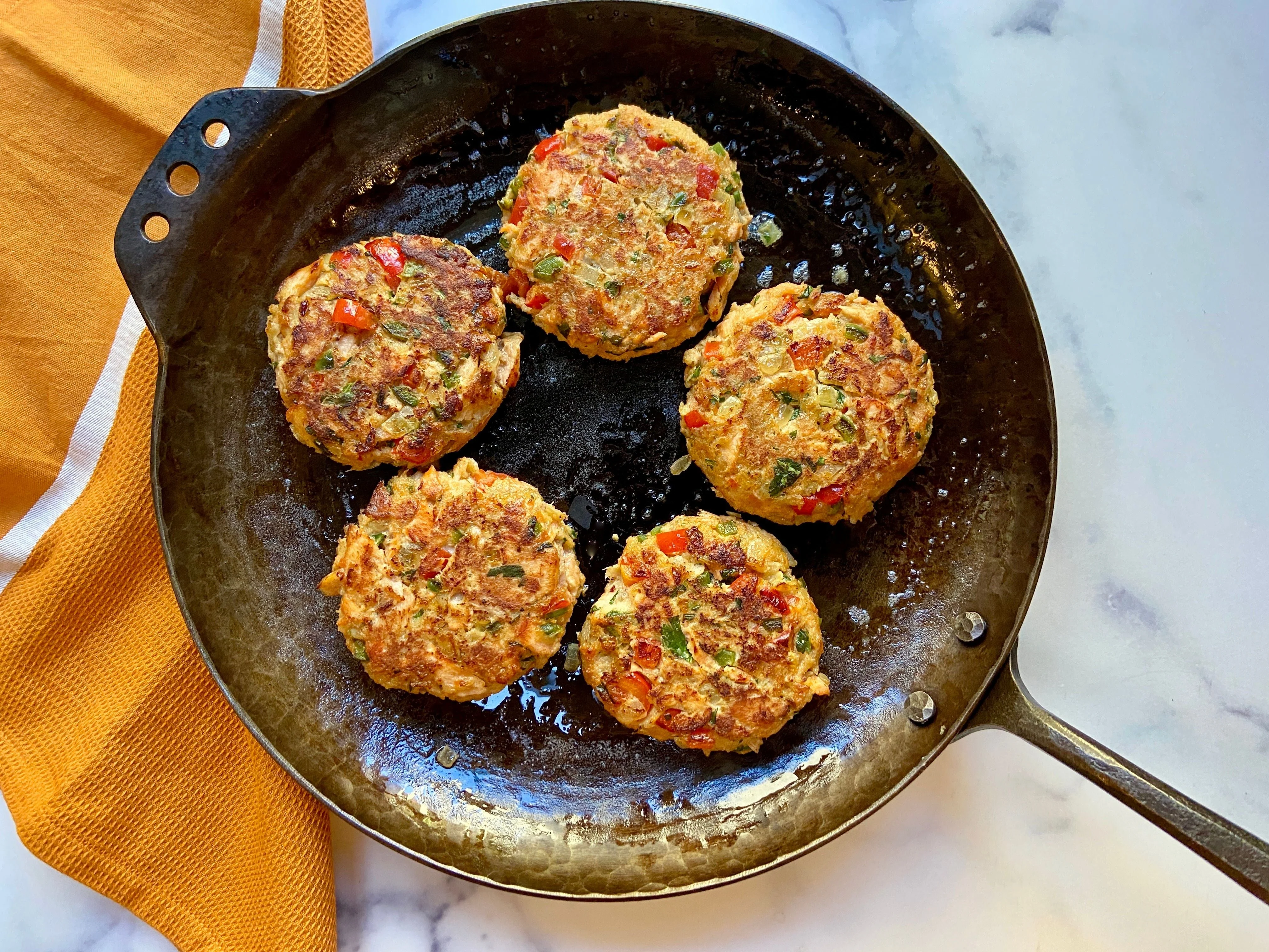 Salmon patties searing in a cast iron skillet with bubbling oil and a thin spatula sliding underneath one patty.
