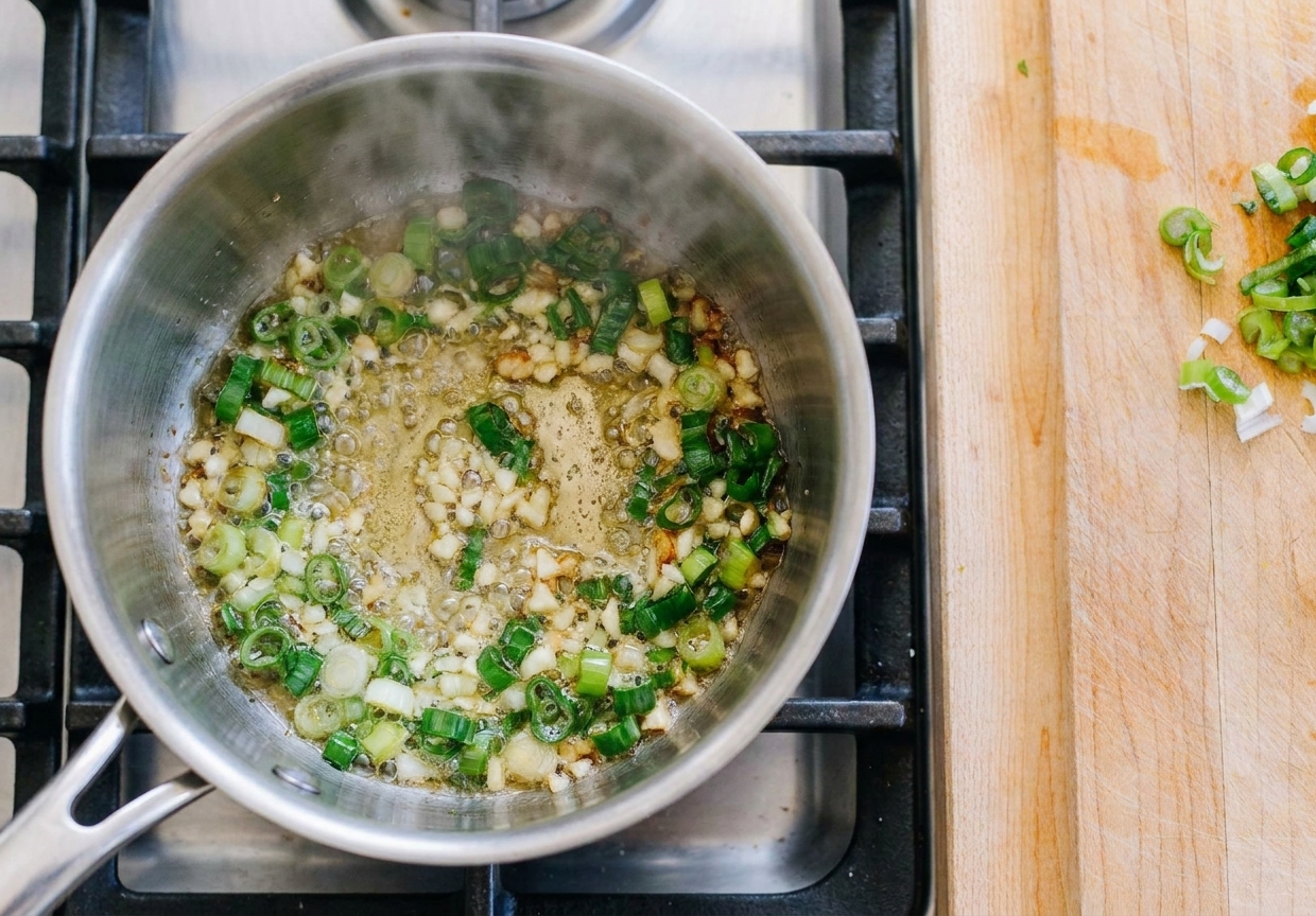 Scallions and minced garlic sizzling in a small saucepan with hot oil on a stovetop