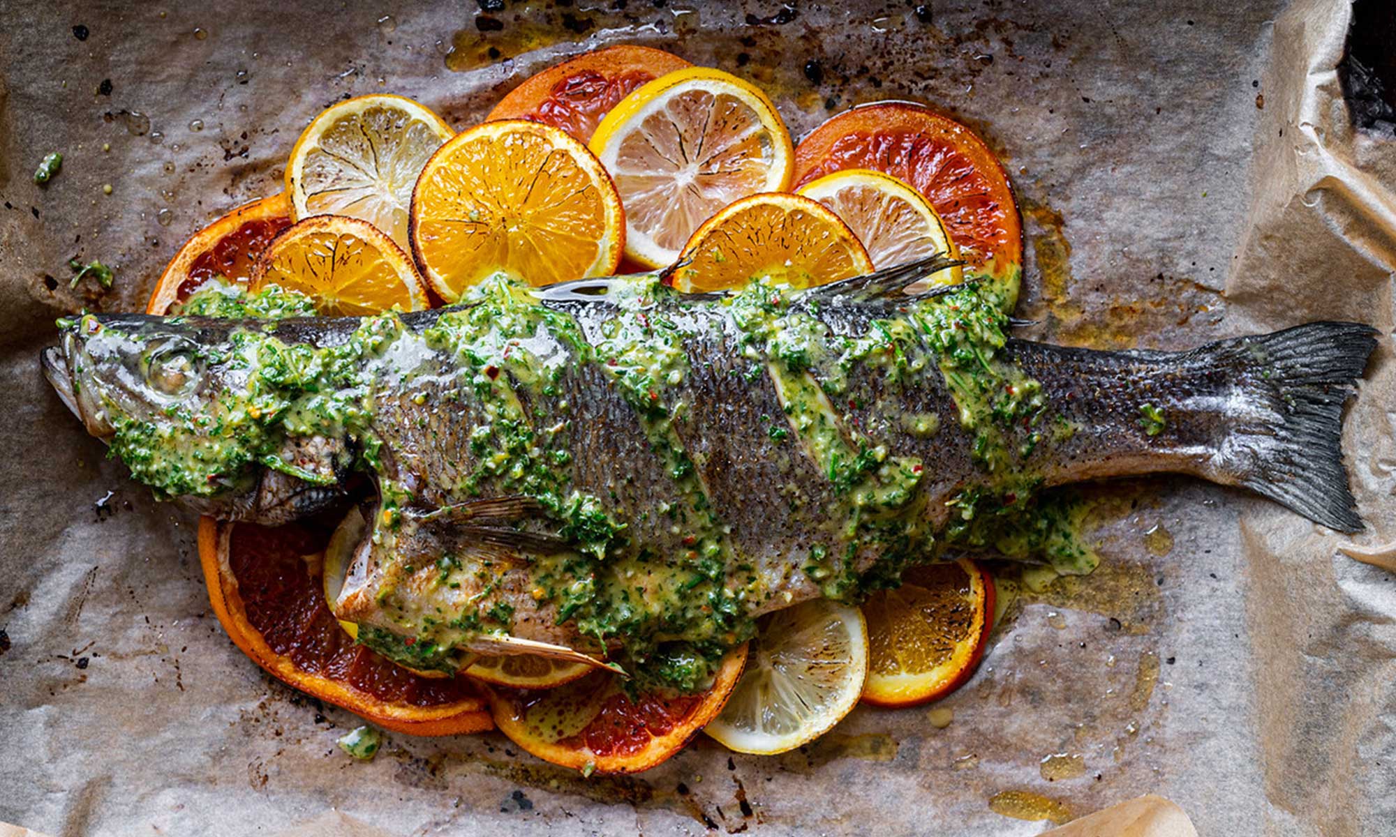 Sea bass cubes sitting in a bowl of lime and orange juice marinade with a spoon resting on the edge on a bright kitchen counter