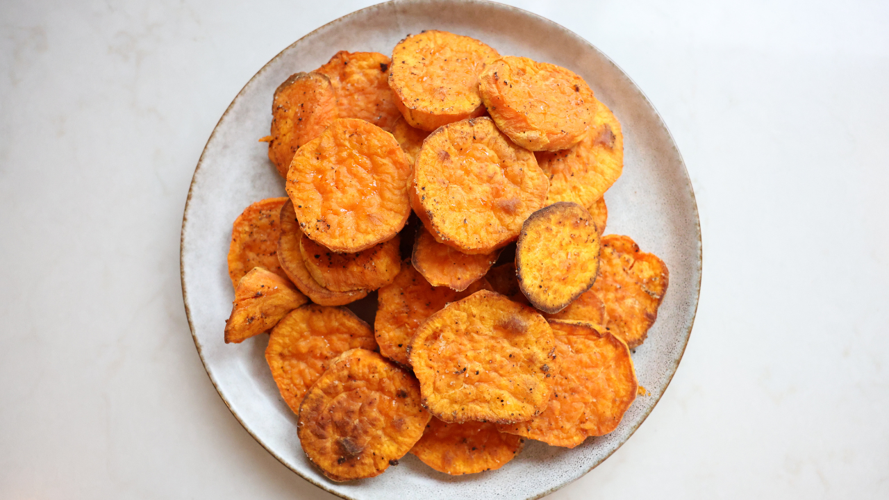 Seasoned Japanese sweet potato rounds coated in olive oil, salt, and pepper in a mixing bowl on a kitchen counter