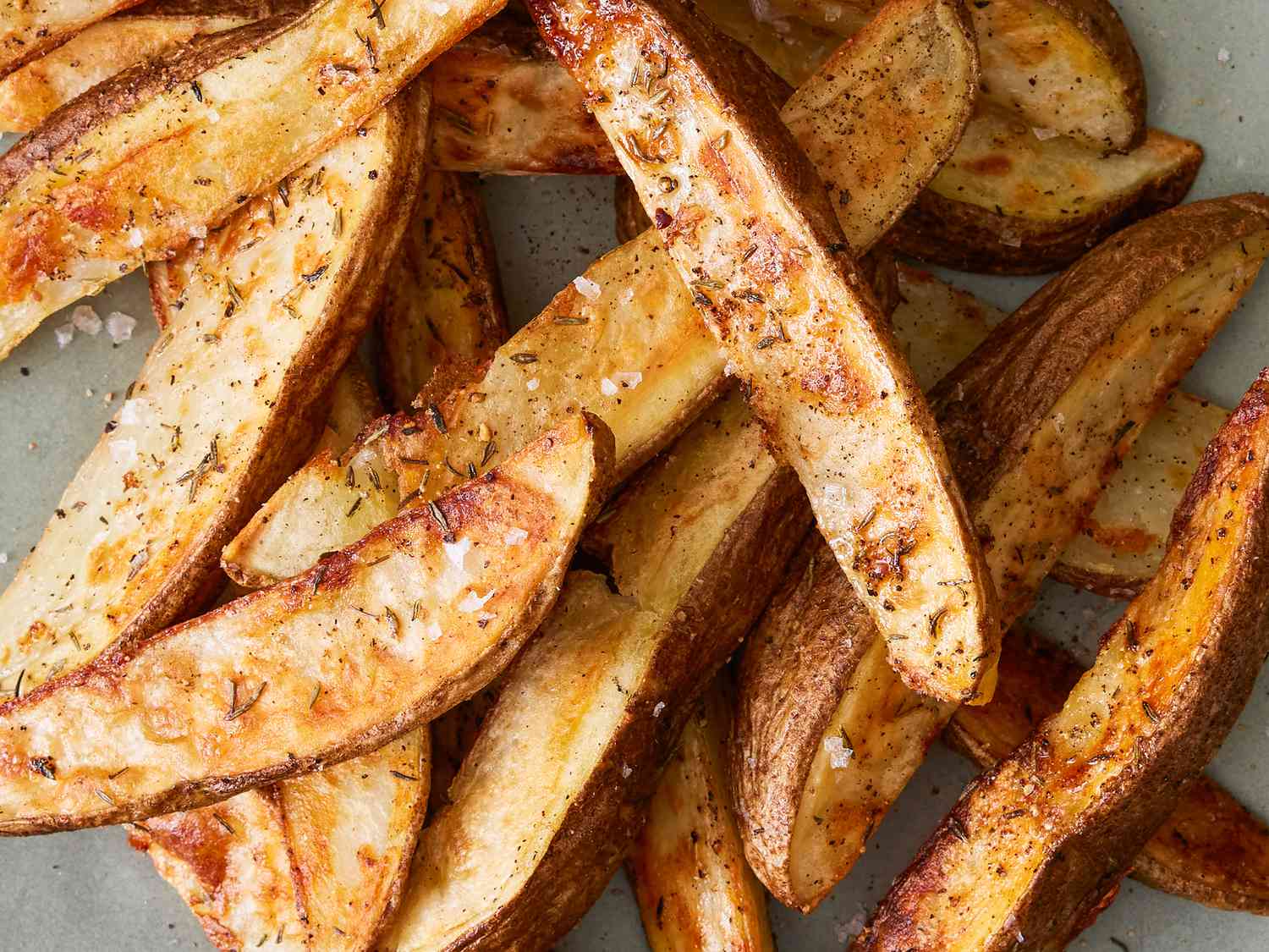 Seasoned raw potato fries spread in a single layer on a parchment-lined sheet pan in a warm home kitchen