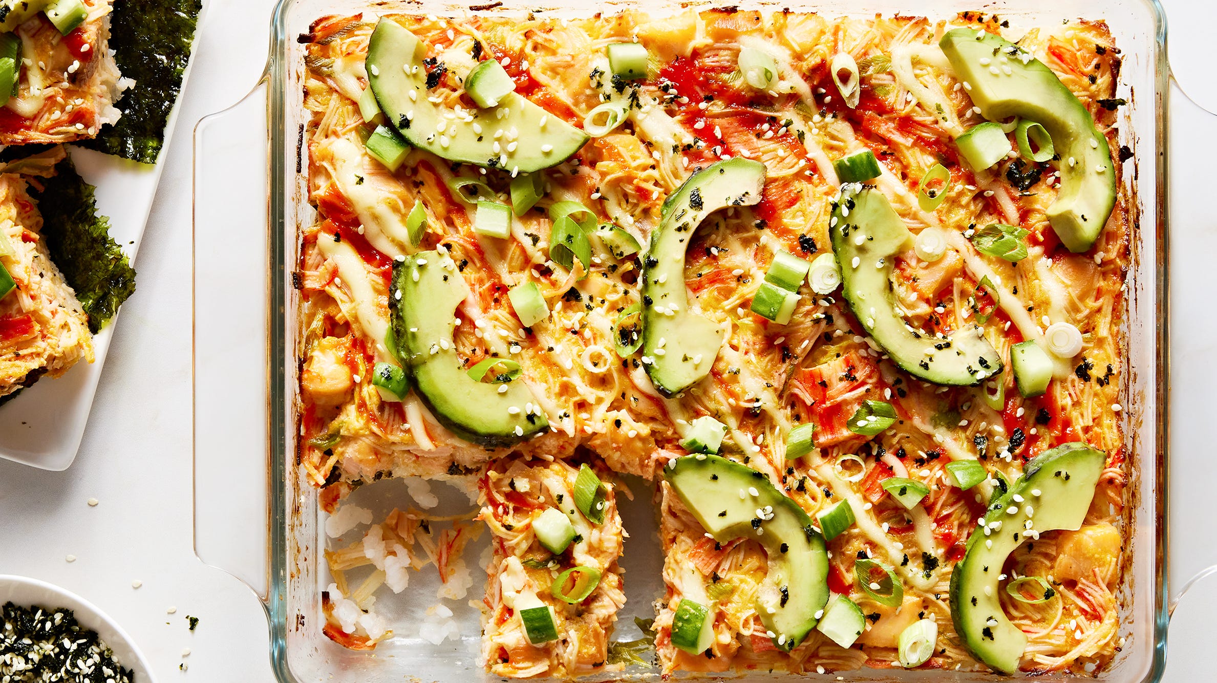 Seasoned sushi rice pressed into an even layer in an 8x8 baking dish on a light kitchen counter