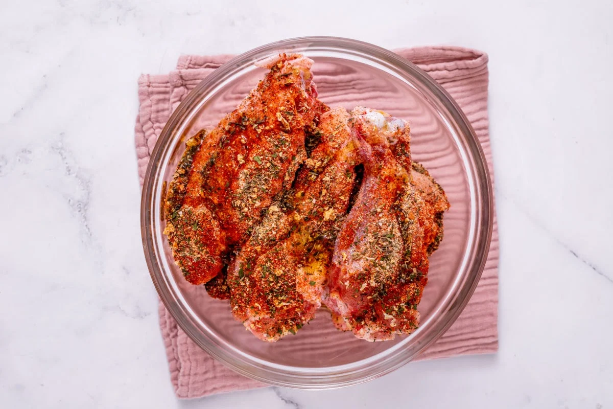 Seasoned turkey wings in a large mixing bowl with visible paprika and herbs coating the skin