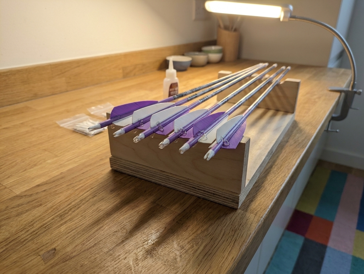 Several freshly fletched arrows resting in a simple rack on a clean table while the adhesive cures