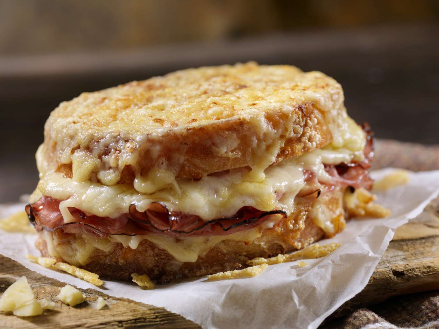 Shredded Gruyère, folded ham slices, and thick-cut bread arranged on a wooden cutting board ready to assemble sandwiches
