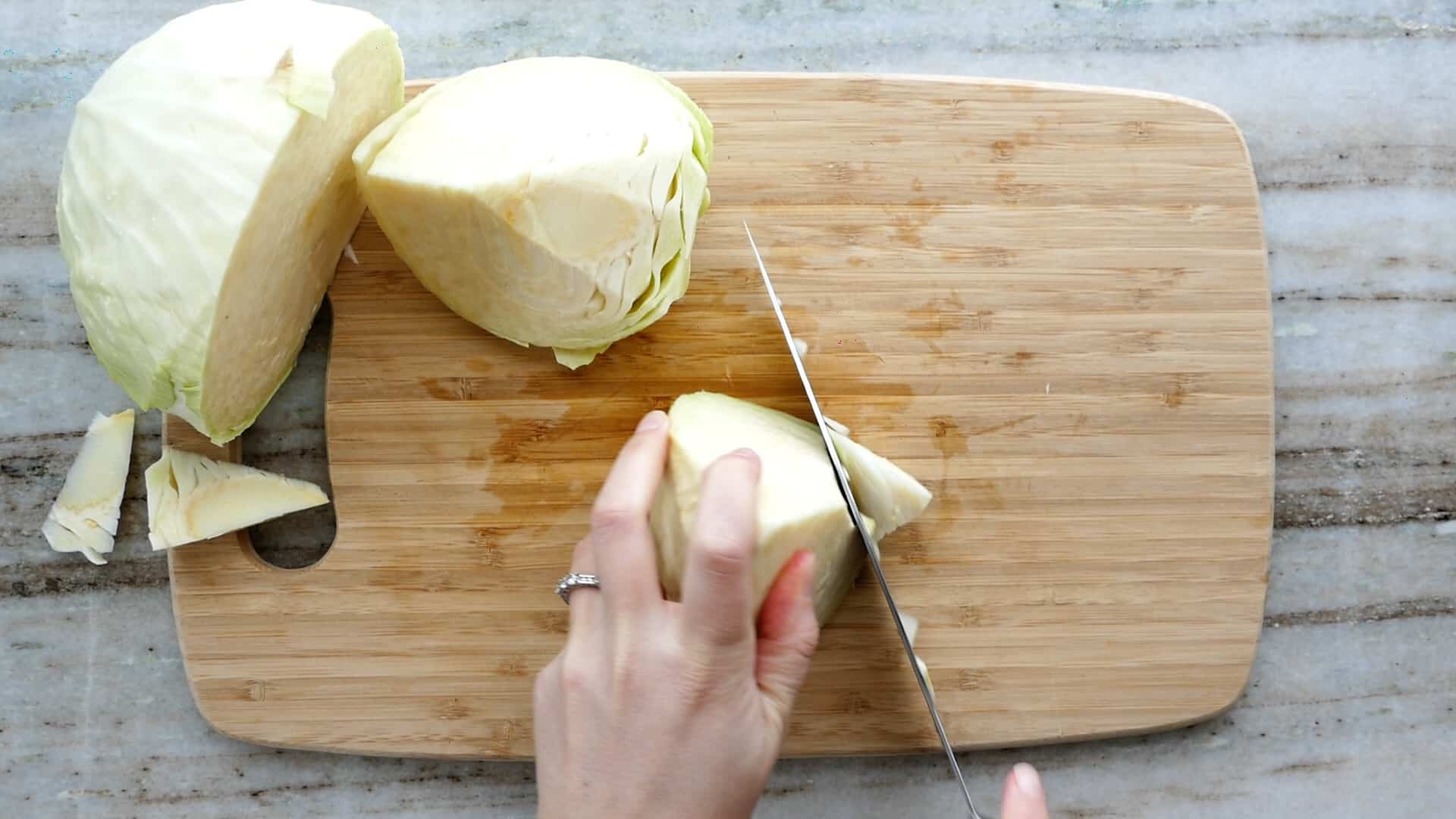 Shredded cabbage and thinly sliced onions on a wooden cutting board with a chef knife on a home kitchen counter