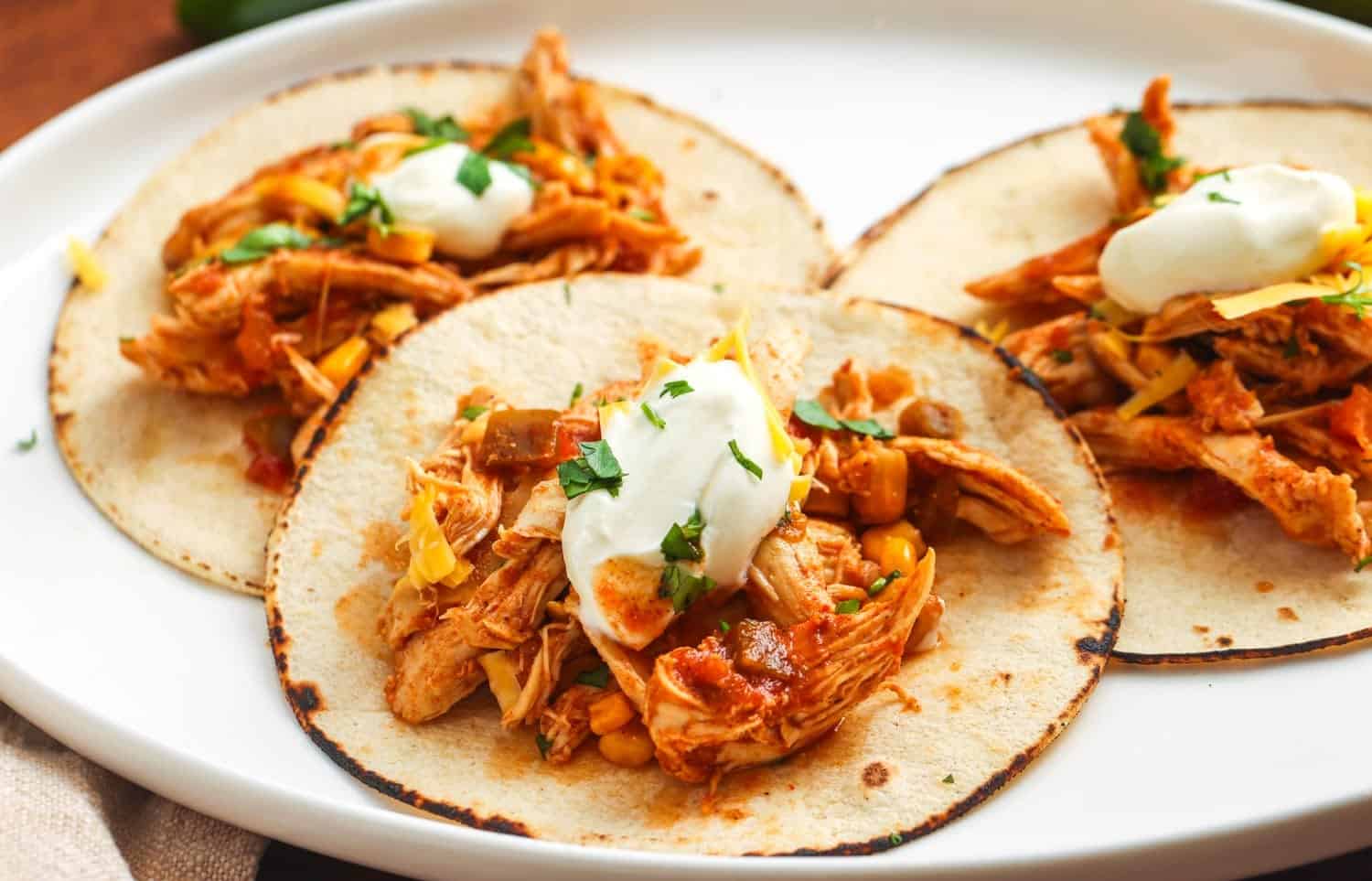 Shredded chicken, shredded cheese, salsa, and large flour tortillas laid out on a kitchen counter ready for assembling chimichangas