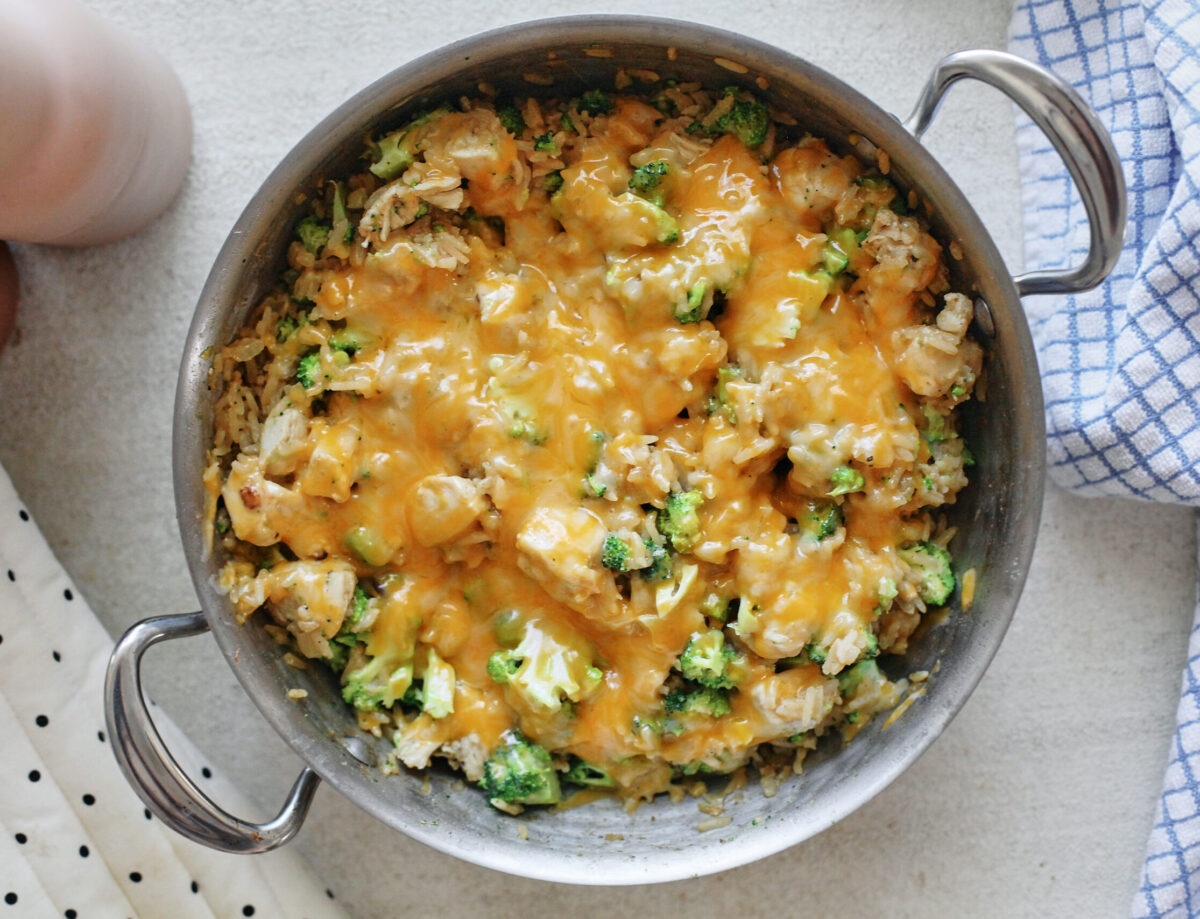 Shredded cooked chicken, broccoli florets, shredded cheddar, and cooked rice arranged in bowls on a neutral kitchen counter