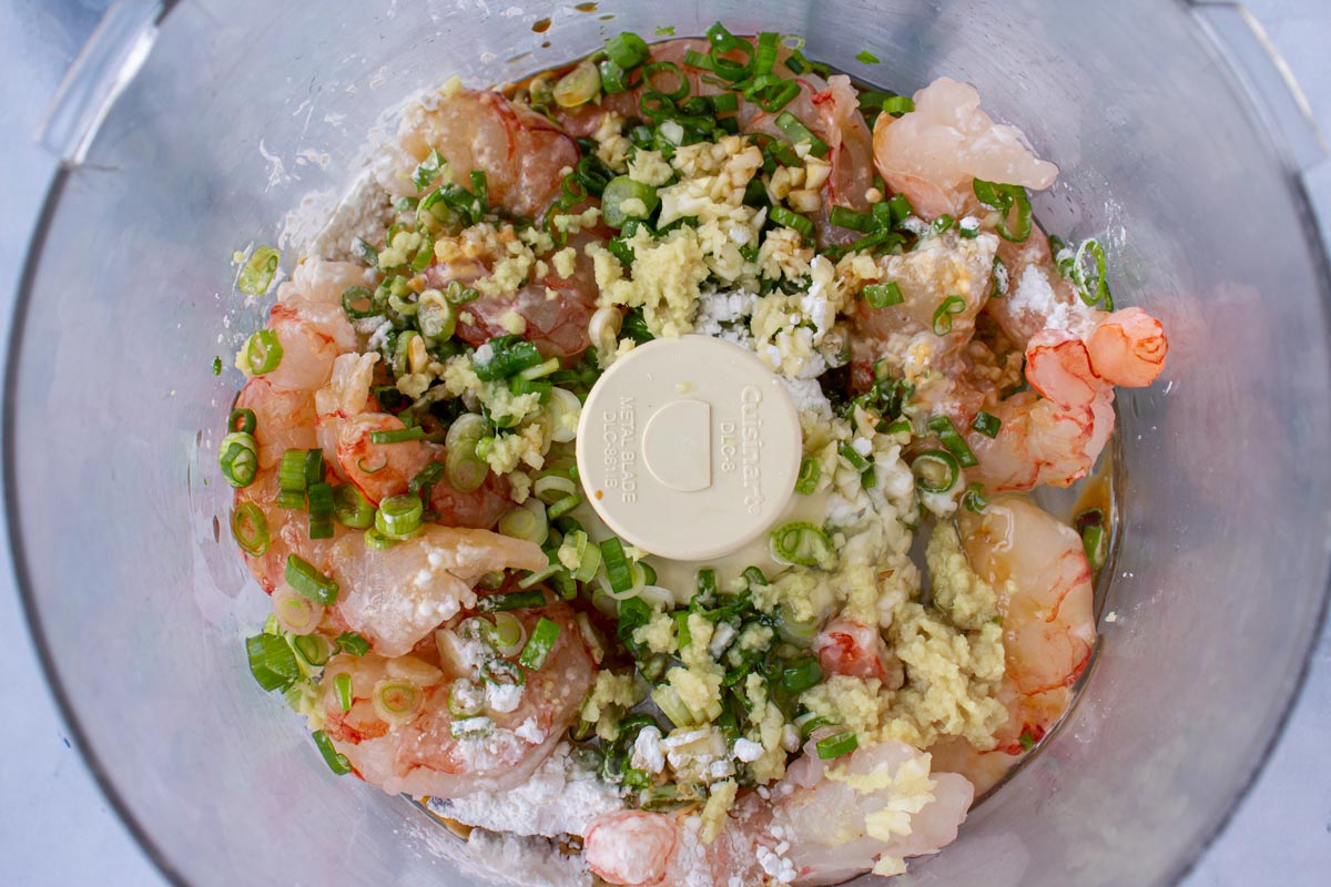 Shrimp mixture being blended into a thick, sticky paste in a food processor bowl on a kitchen counter