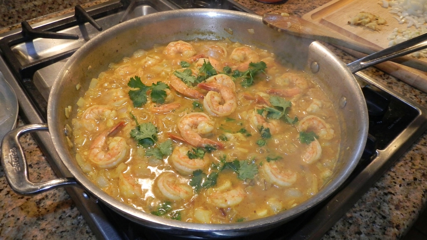Shrimp simmering in a bubbling coconut curry sauce in a large skillet on a home stove
