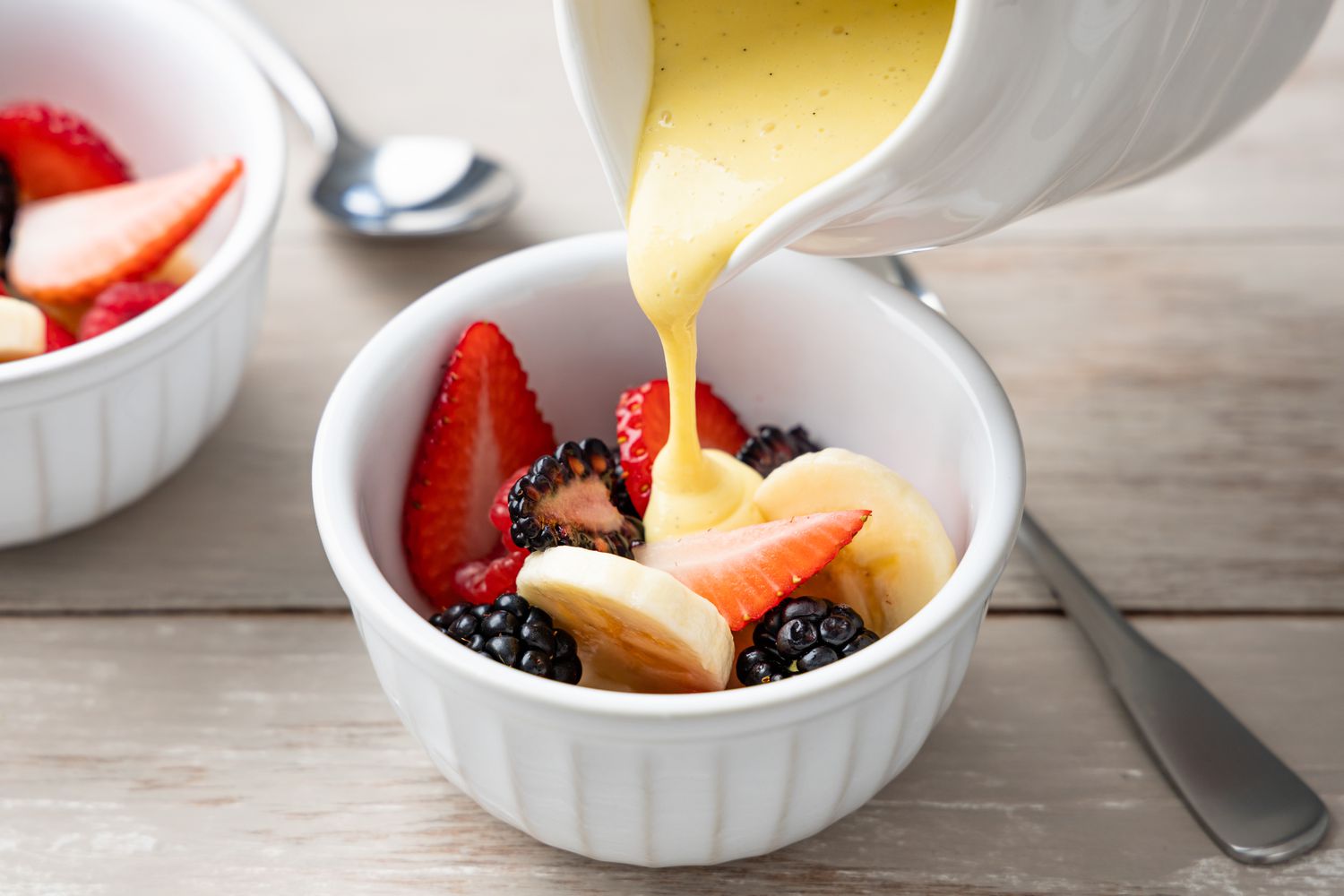 Silky vanilla custard in two small glass bowls on a warm kitchen table, topped with a few fresh berries, soft natural window light